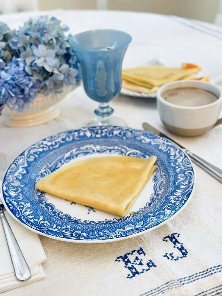 Vintage table setting on antique French monogrammed linen with blue and white transferware, an opaque blue glass, and a café au lait cup