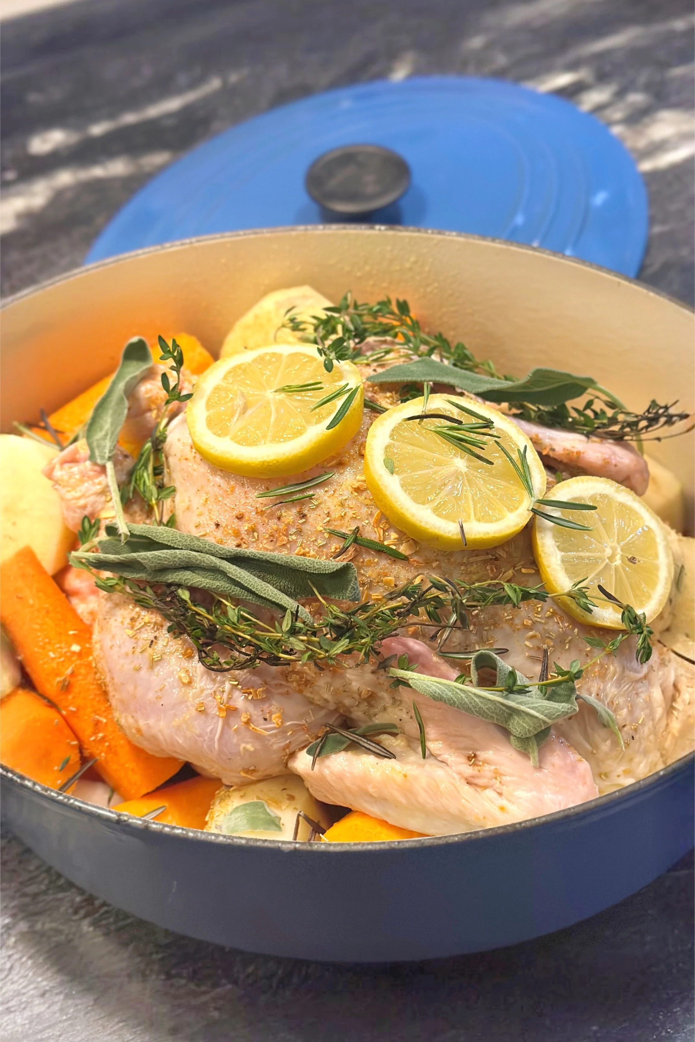 French roast chicken with fresh herbs lemon and root vegetables in a blue Le Creuset roasting pan ready for the oven — Merze Lifestyle Sunday slow living recipe