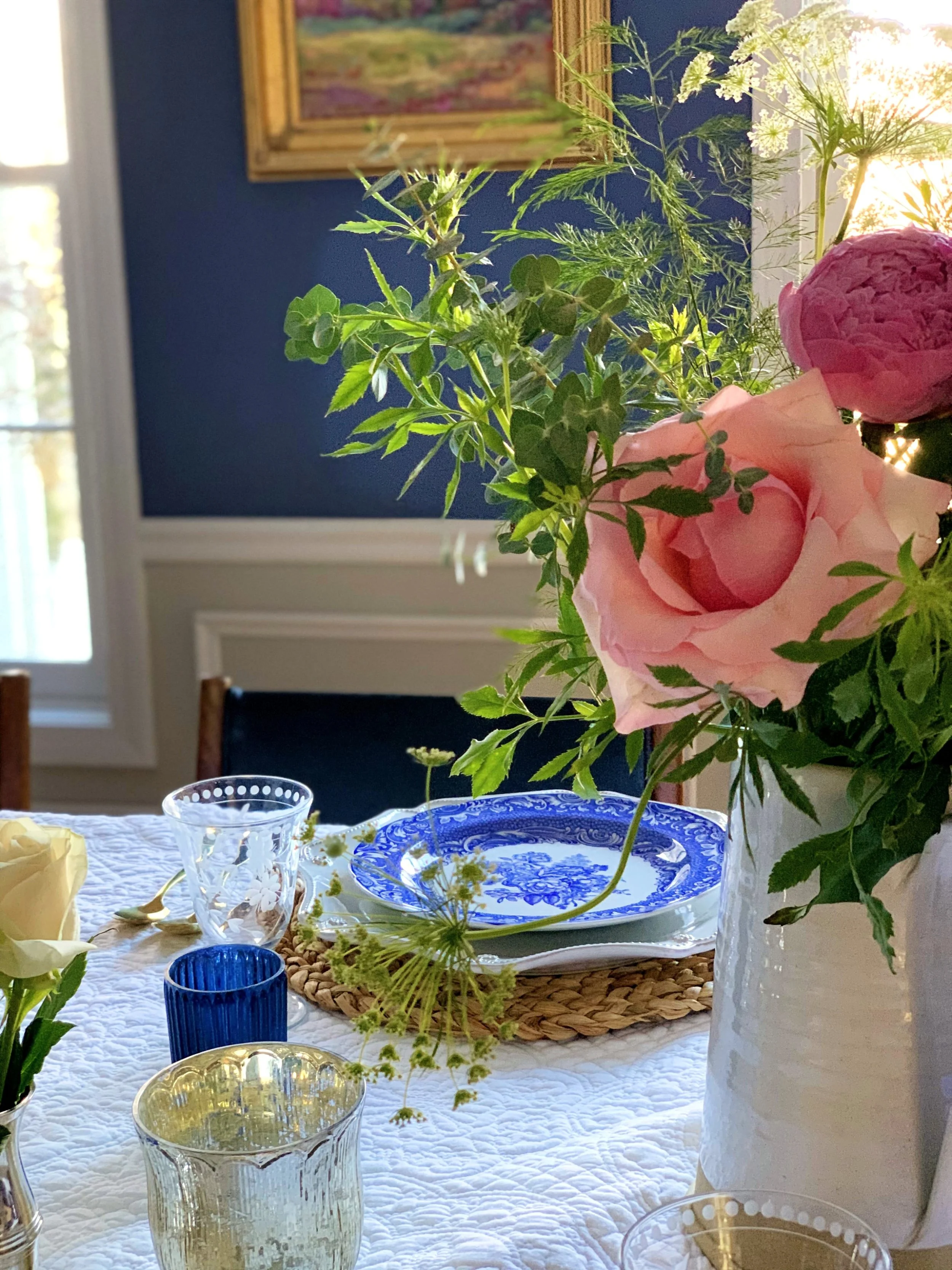 A cream blanket with raised stitching used as a tablecloth beneath blue and white china and garden roses