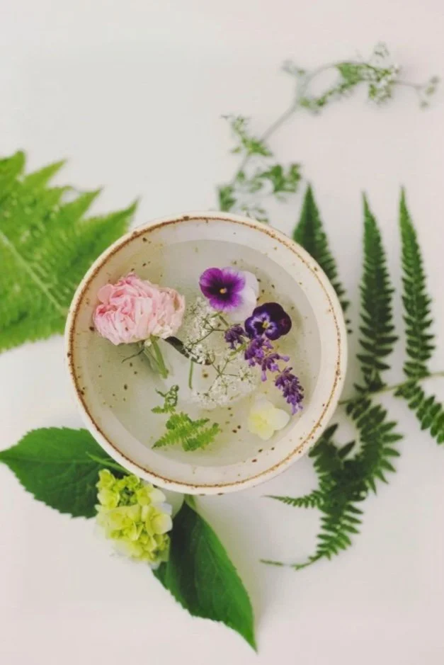 Flatlay of hydrangeas, ferns, and garden flowers resting in water in a bowl before arranging.