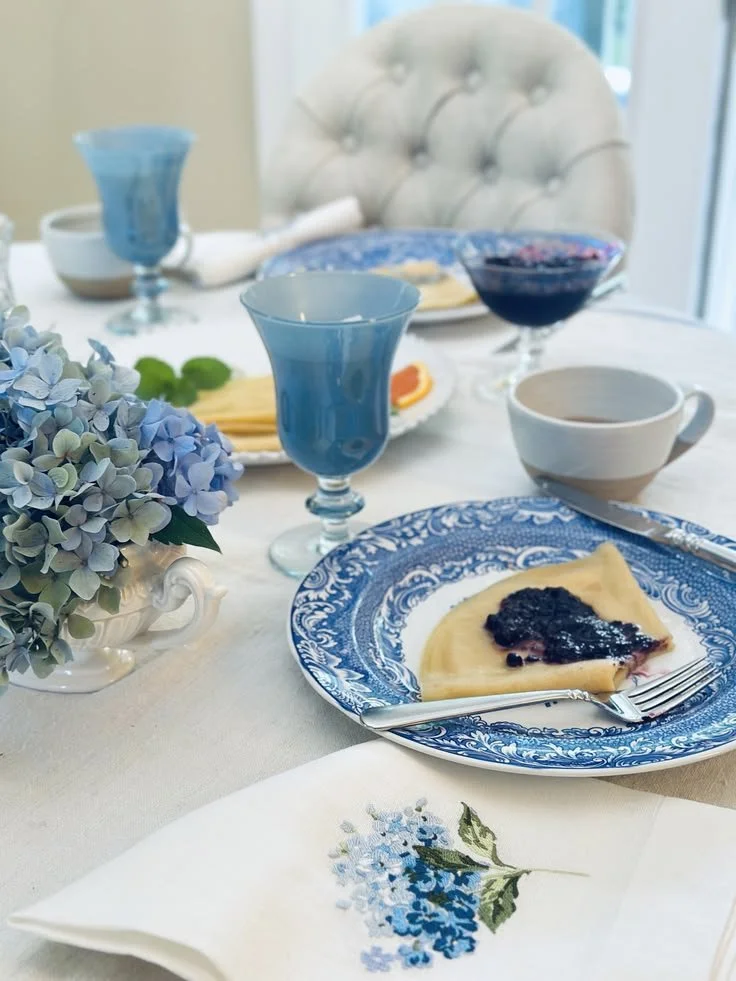 Blue hand-blown wine glass on a French linen brunch table with blue and white transferware and hydrangeas