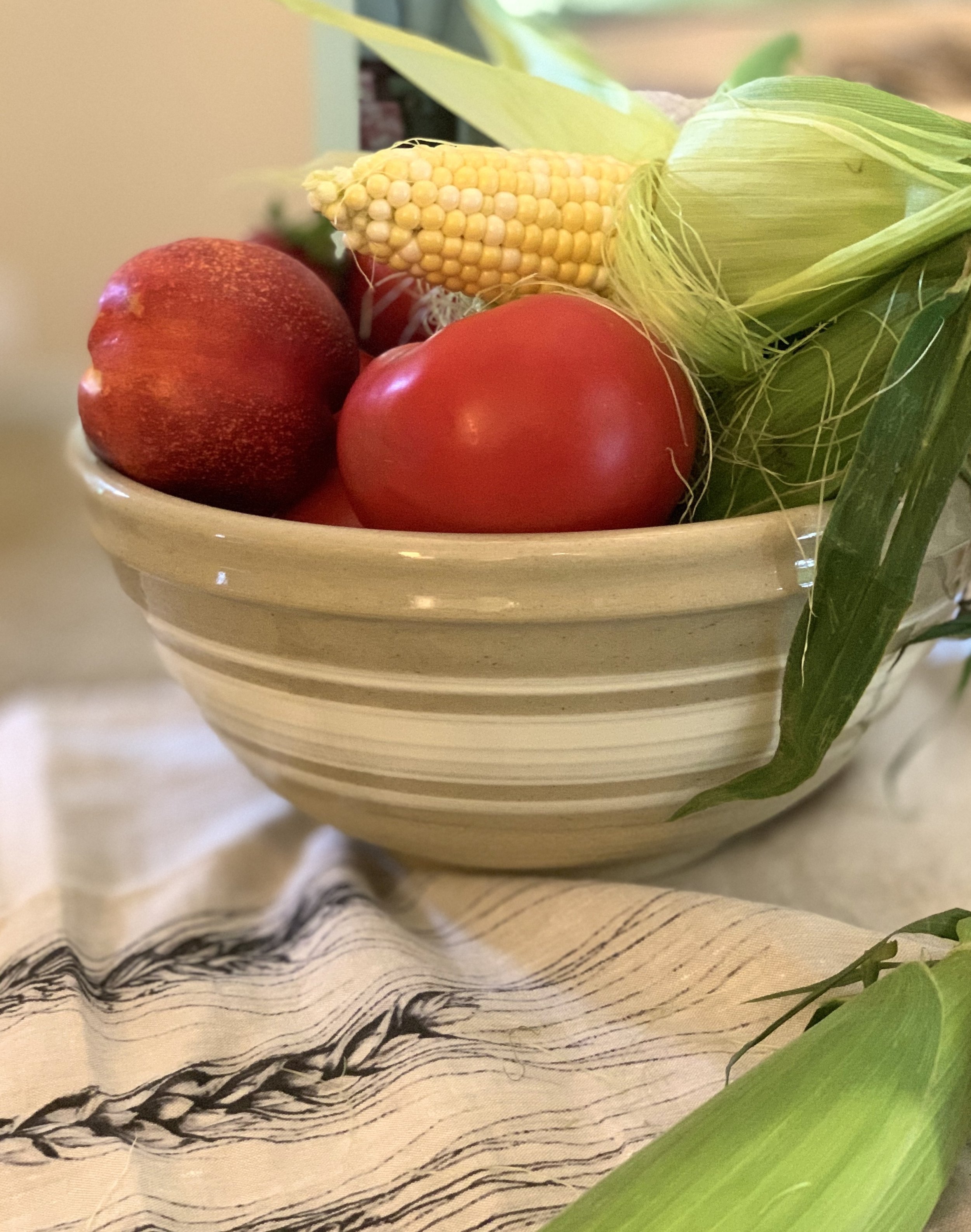 Handmade yellowware bowl filled with fresh summer corn, tomatoes, and nectarines on a French linen tea towel, from MERZE Lifestyle.