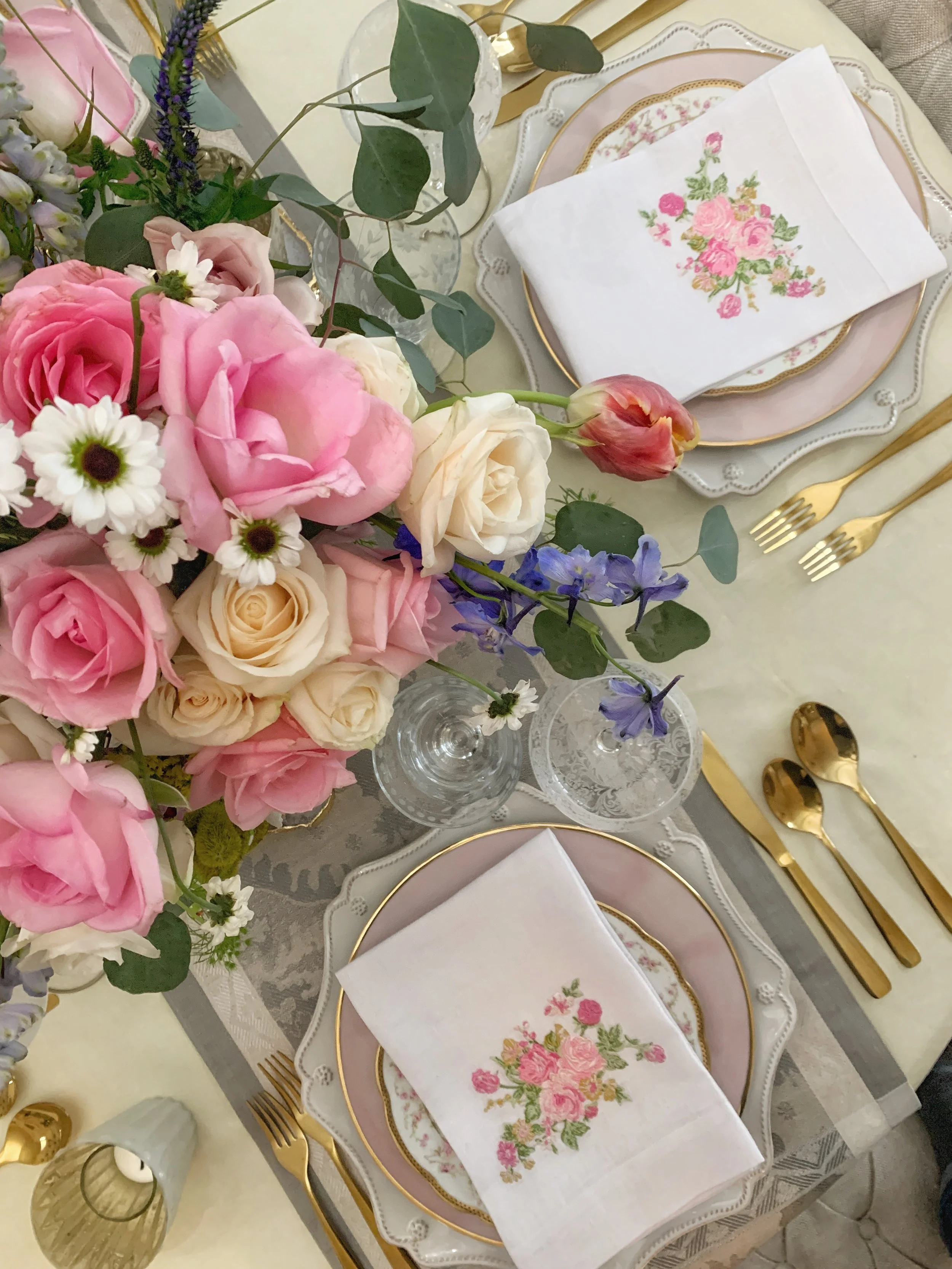 Aerial view of two Easter place settings with mixed china, embroidered linens, and a full spring floral arrangement of tulips and hyacinths.