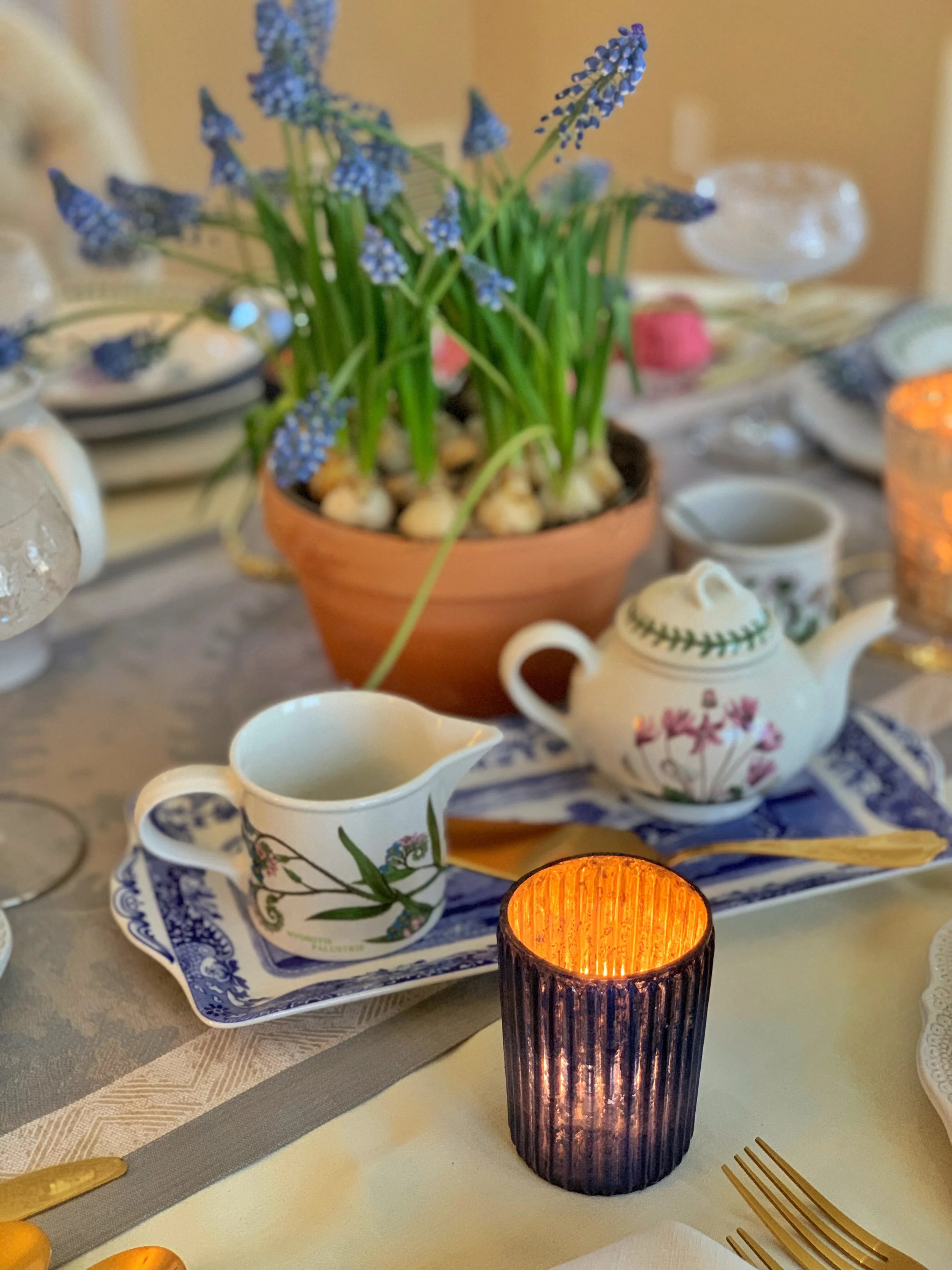 blue votive candle with cream and sugar set on blue and white platter and grape hyacinth centerpiece on linen runner