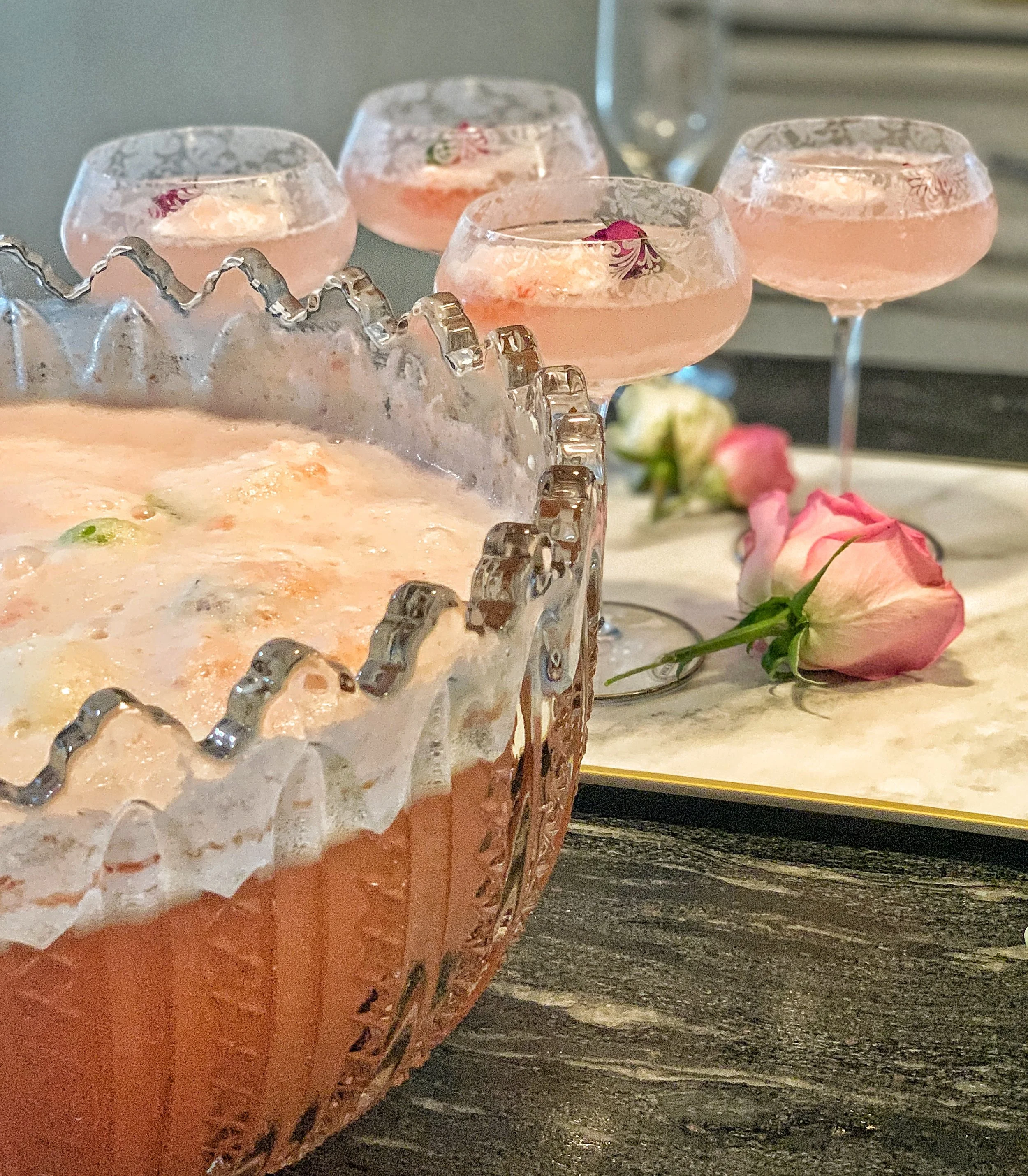 Inherited cut glass punch bowl with rose-infused sherbet punch, surrounded by etched wine glasses filled with a floral spring drink and styled on a marble tray with fresh roses.
