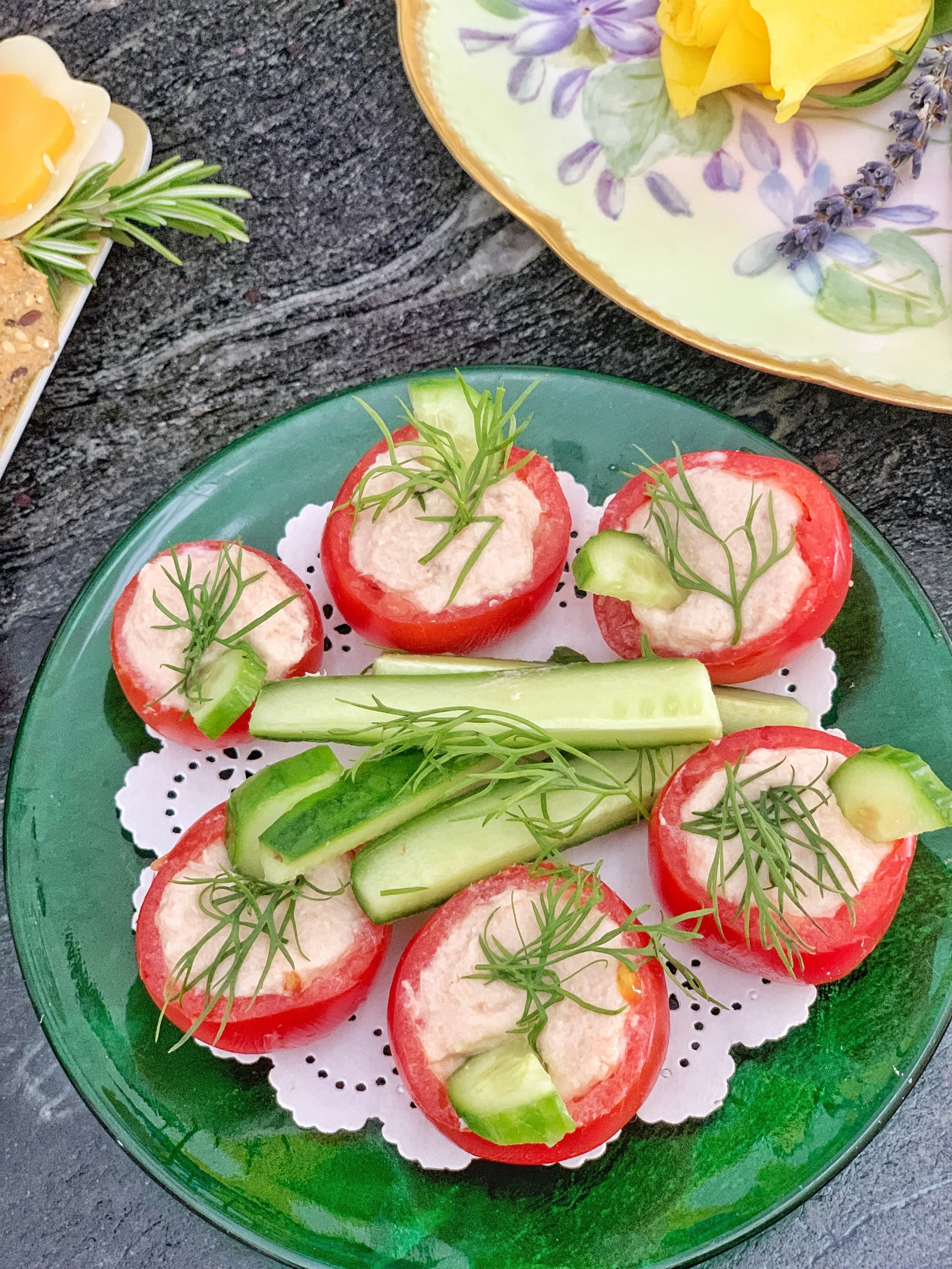 Miniature tomatoes filled with tuna, dill, and cucumber salad, garnished with fresh dill and served on a green antique glass plate for a spring Easter appetizer.