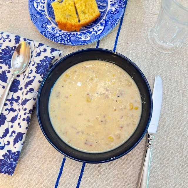 Bowl of roasted corn chowder with cornbread on a blue and white plate, set on a linen runner