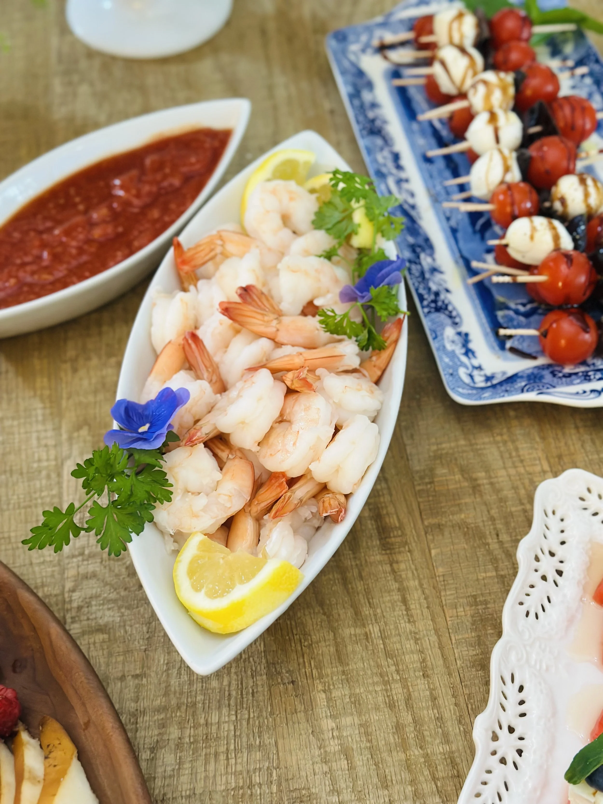 Easy shrimp cocktail in a white boat dish garnished with parsley, lemon, and an edible viola, served with cocktail sauce.