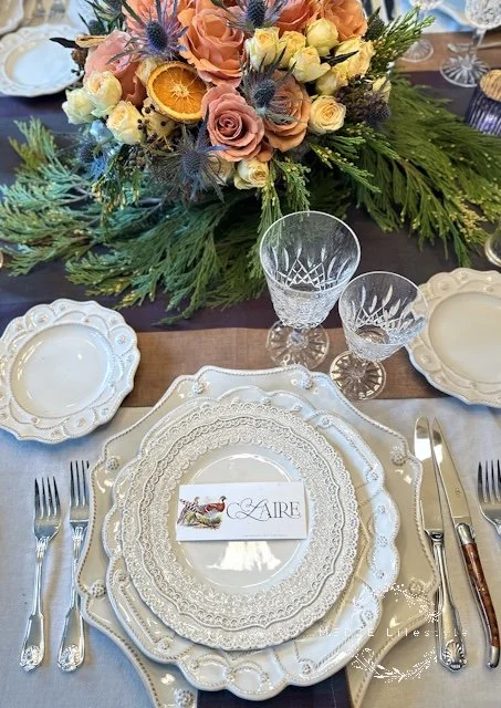 Cream layered place setting with subtle patterned plates, sterling silver flatware, crystal glassware, and floral centerpiece detail in a quiet luxury tablescape