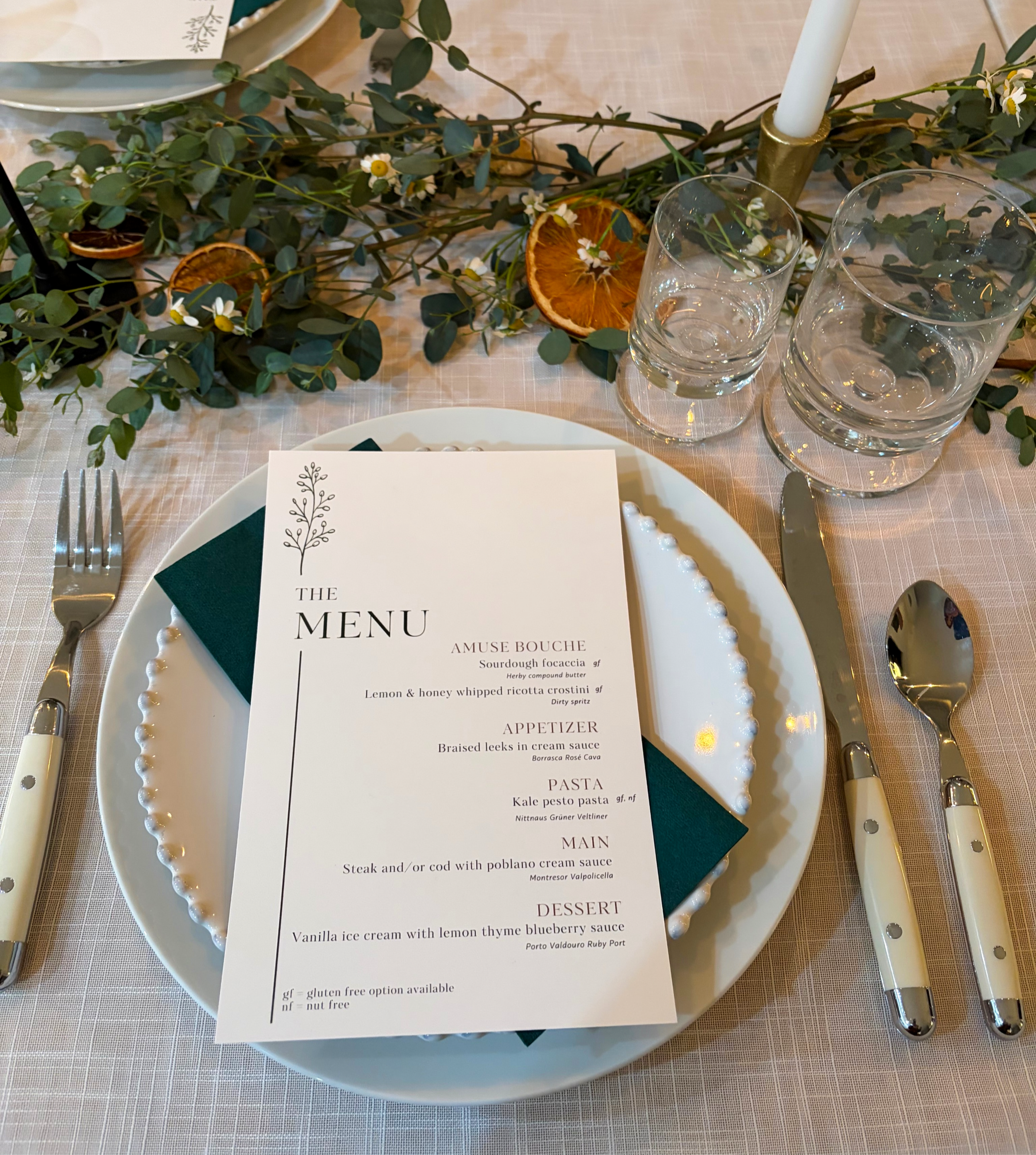 Printed multi course dinner menu with wine pairings placed diagonally on a formal table setting.