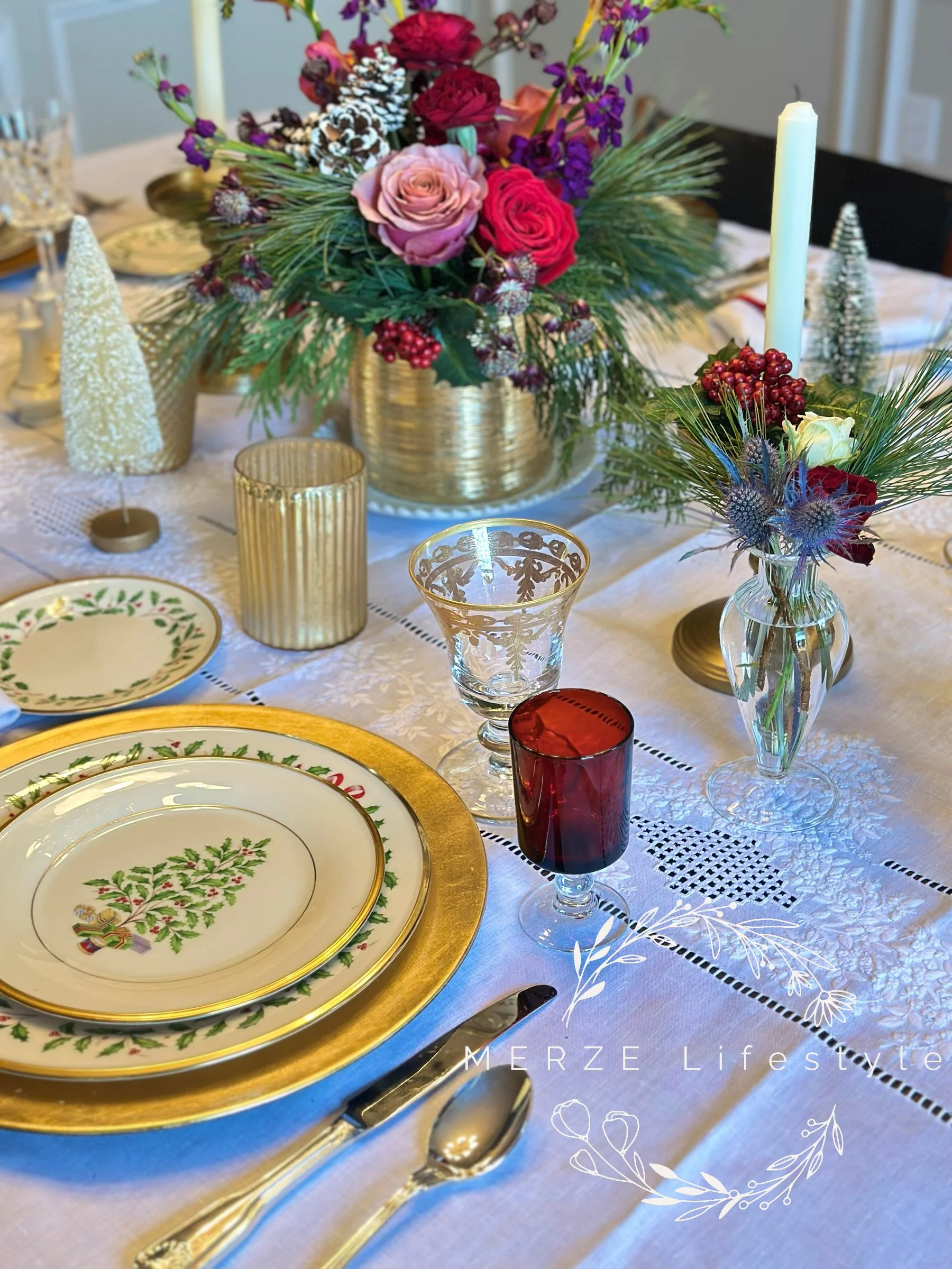 Elegant holiday table setting with layered place settings, red glassware, gold accents, and a refined red, green, gold, and white color palette.