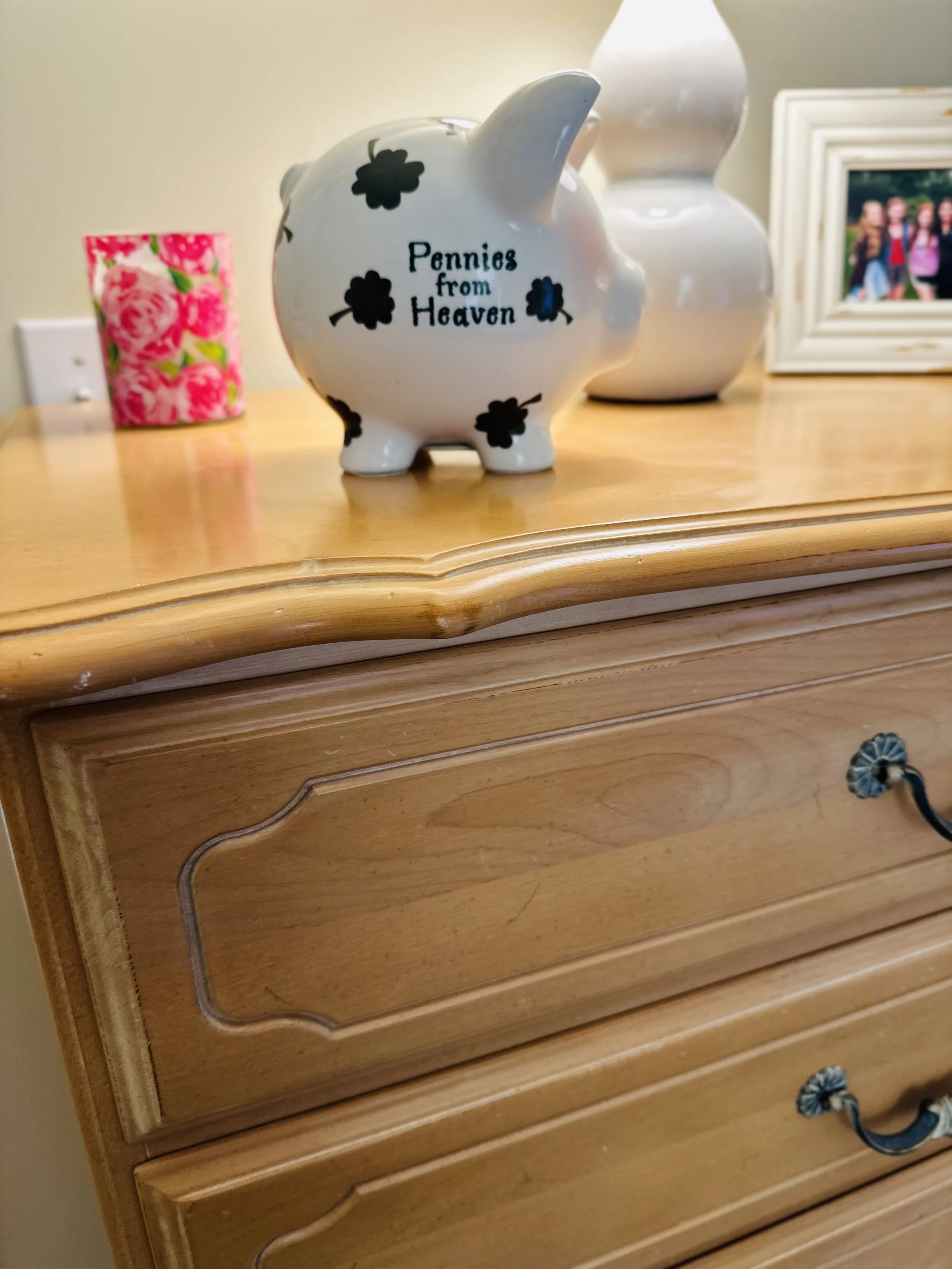 A dresser-top vignette with a childhood piggy bank, framed photographs, and a candle, arranged on a painted birch chest.