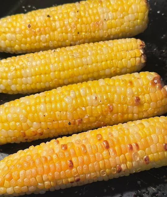 Four ears of fresh corn roasted until lightly charred on a dark baking pan