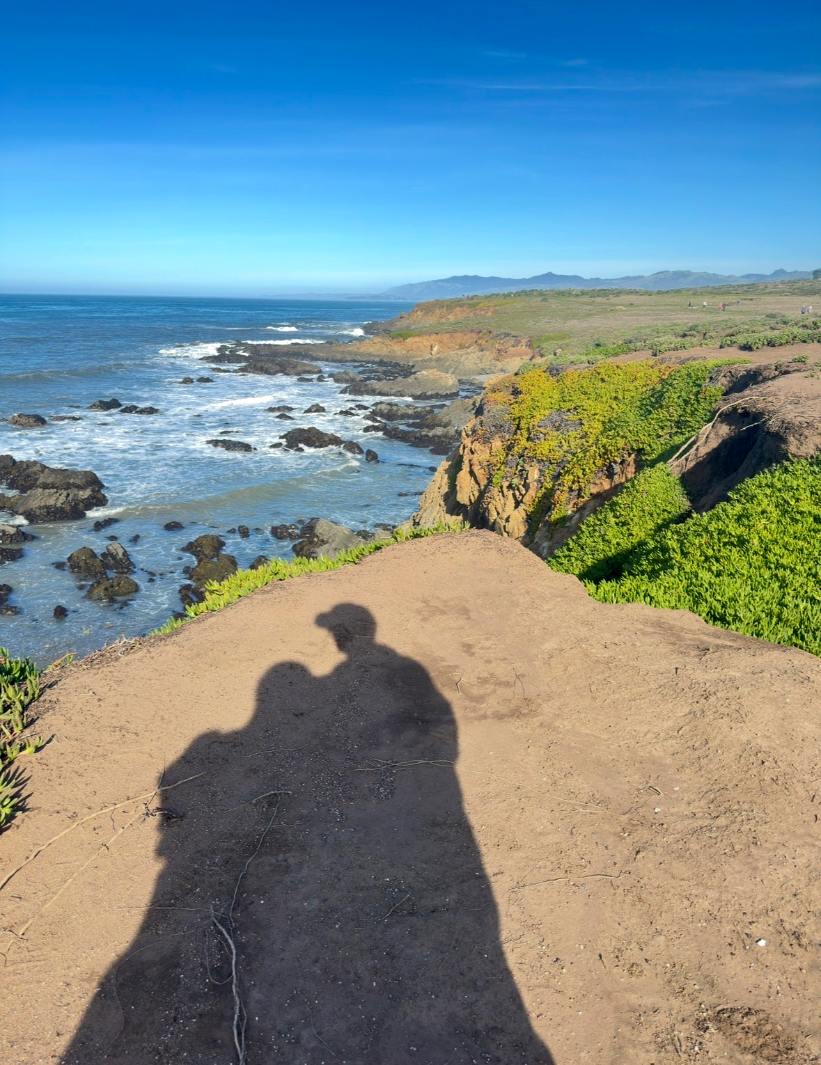 Silhouette shadows of a couple standing on coastal cliffs overlooking the Pacific Ocean at sunset, reflecting transition and shared restoration.