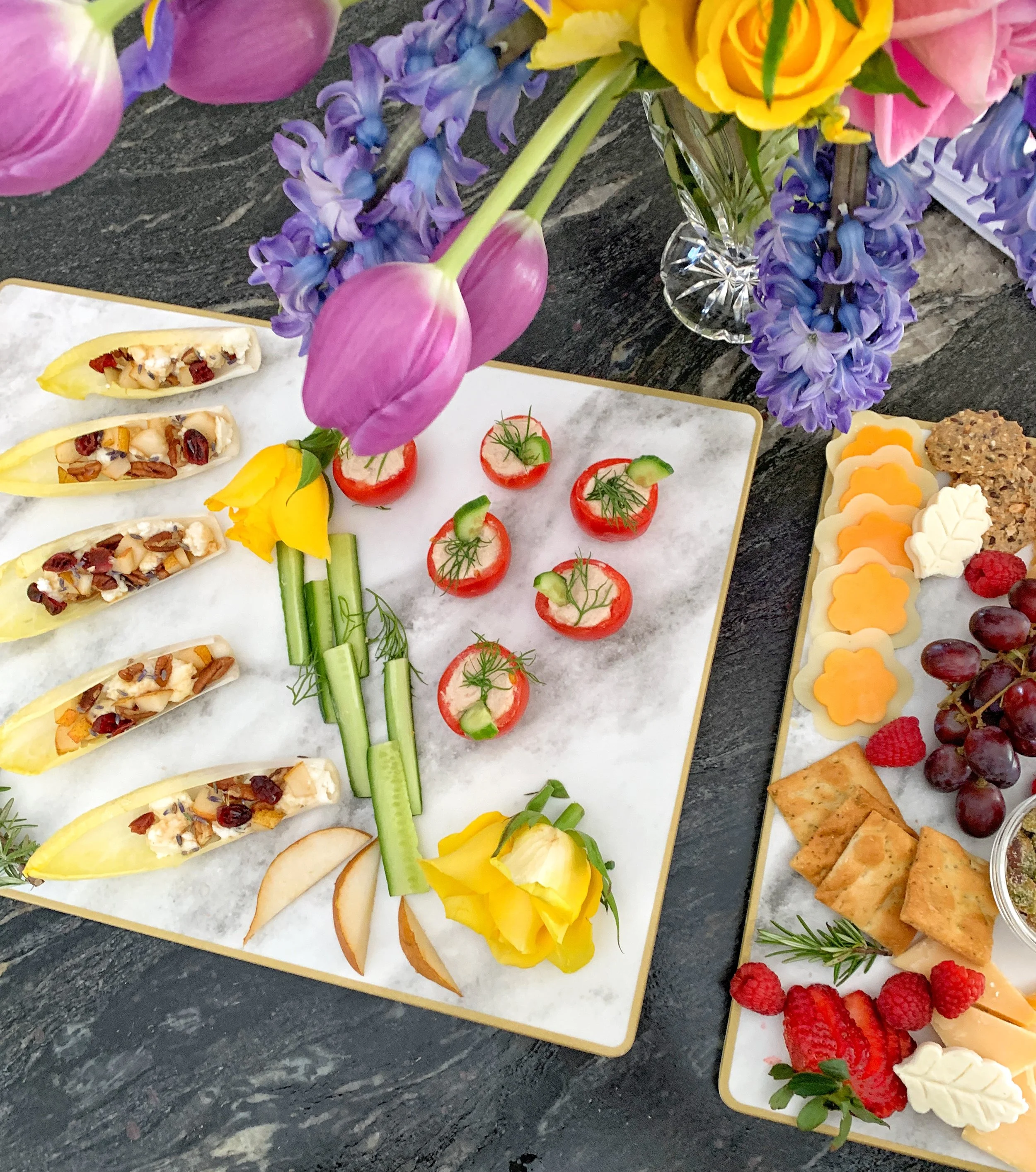 Overhead view of an Easter charcuterie board and appetizers styled on a marble platter with fresh hyacinths and tulips for a spring gathering.