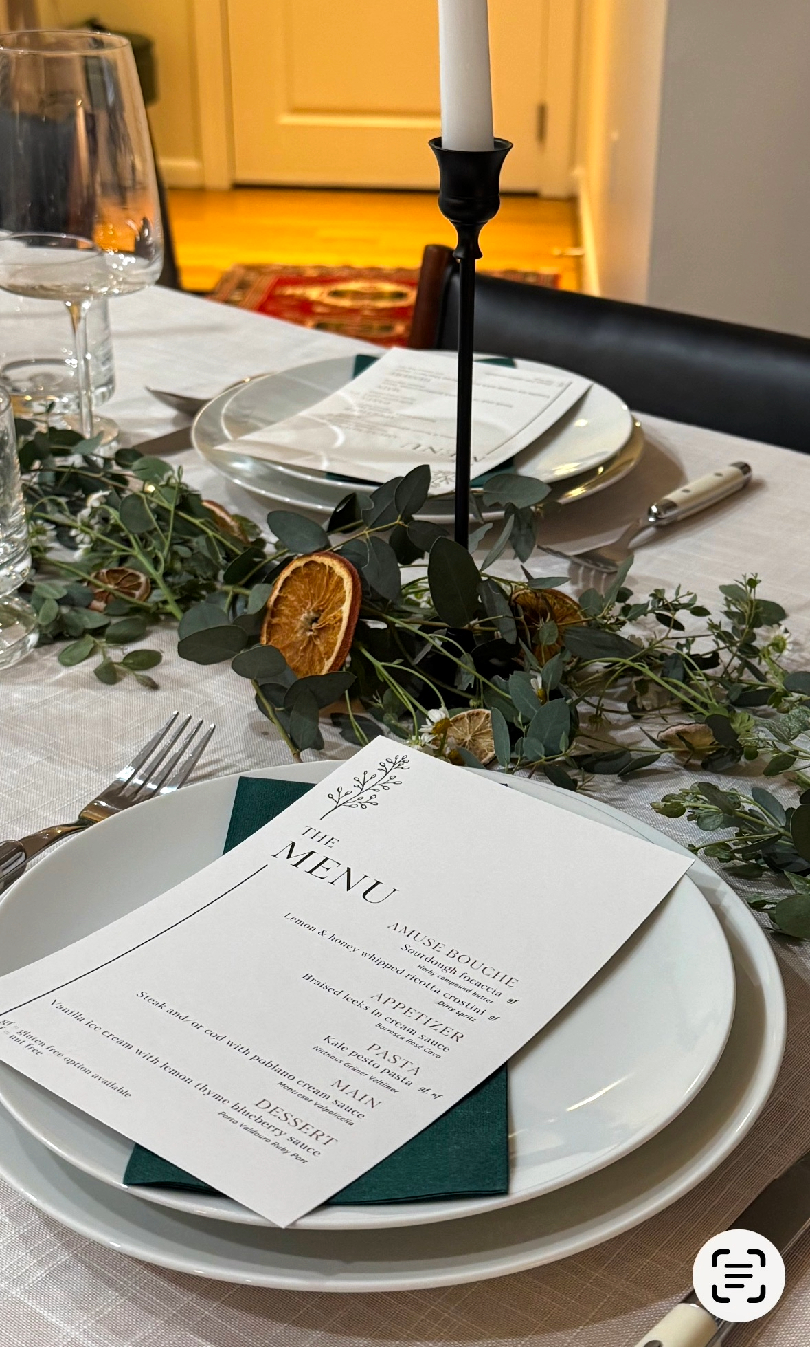 Close up of table centerpiece featuring eucalyptus, chamomile flowers, and dried orange slices on a linen tablecloth.
