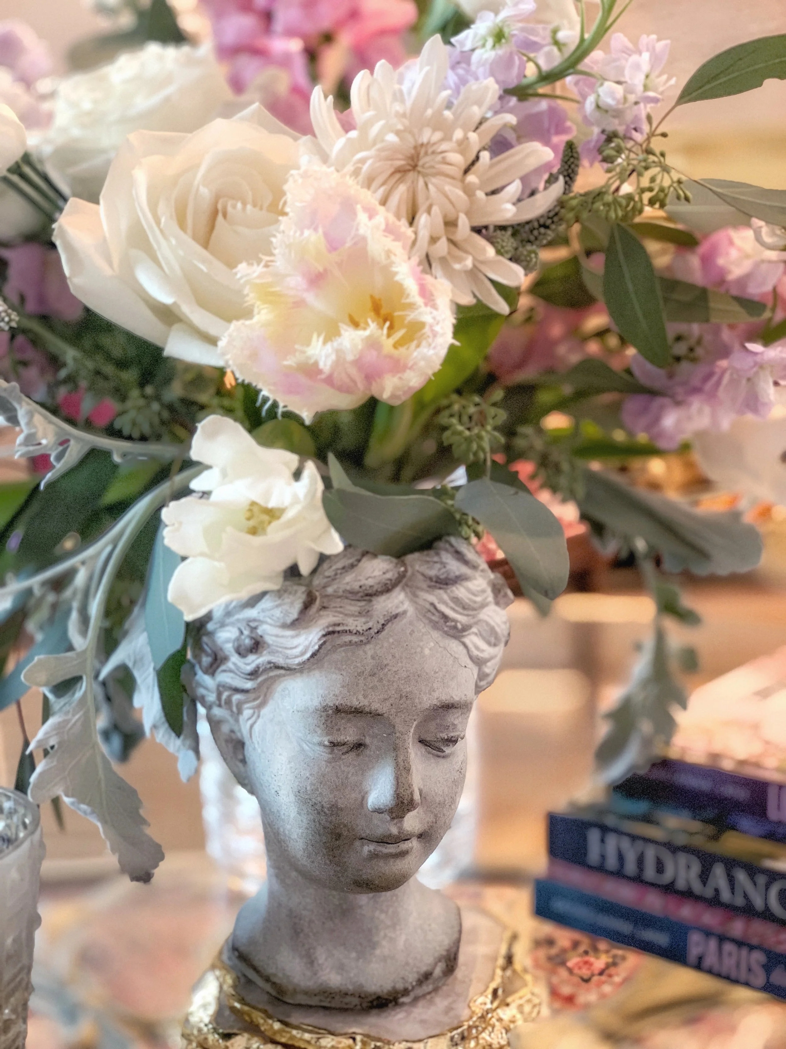 Greek ceramic bust vase filled with spring flowers styled on a glass table alongside London in Bloom by Georgianna Lane as a decorative spring entertaining vignette
