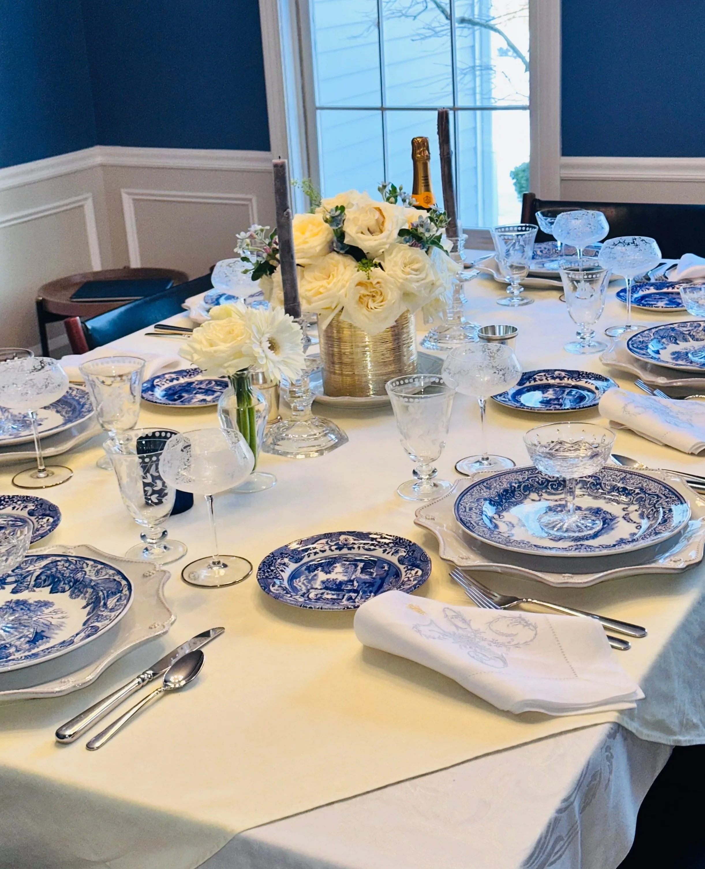 Blue and white dining table in a room with soft blue walls, cream painted wainscoting, and natural light from the outdoors.