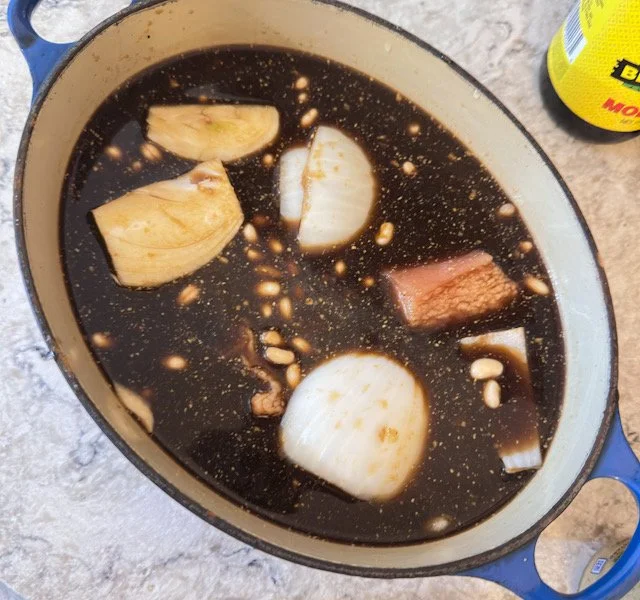 Navy beans in molasses with quartered onion and salt pork in a Le Creuset pot before baking