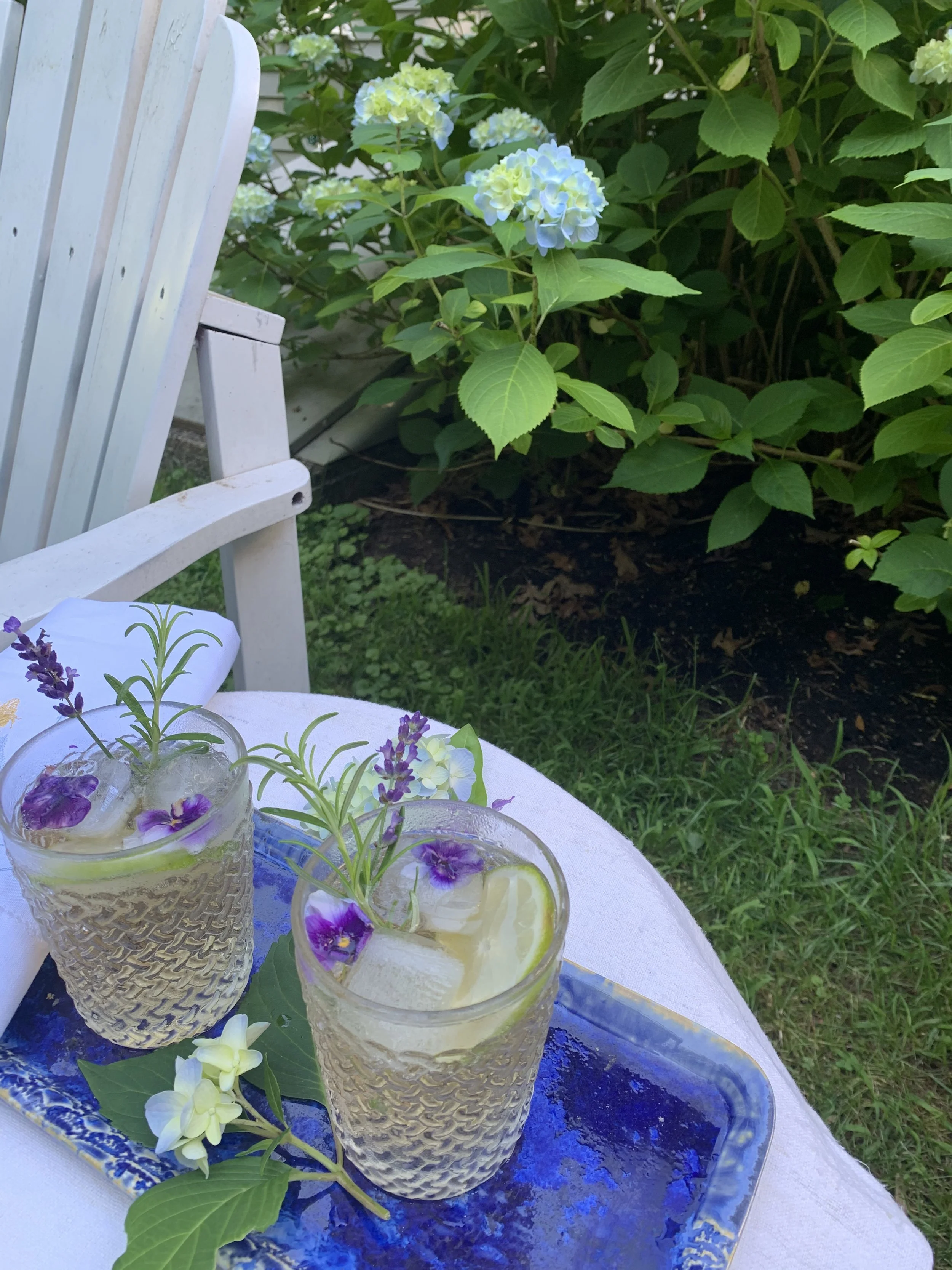 Textured glass with rosemary and lavender, violas frozen in the ice, on a blue tray beside blooming hydrangeas