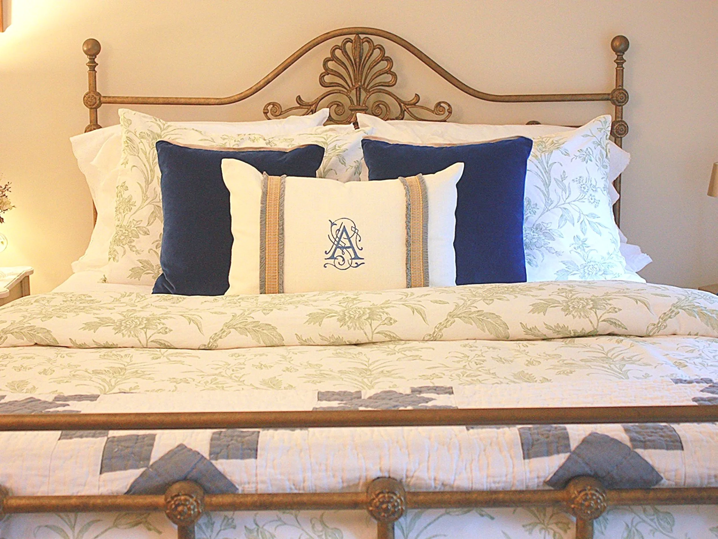 A close-up of a vintage iron bed headboard layered with toile bedding in a soft French inspired bedroom.