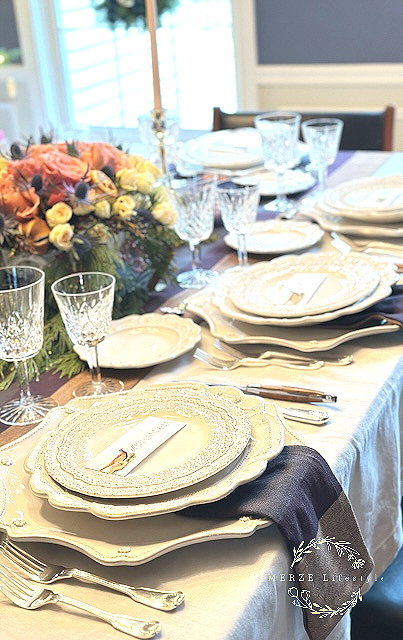 Layered cream plates with sustainable woven napkins and runner cascading between charger and upper plate in a traditional neutral tablescape.