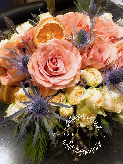 Seasonal floral arrangement with dried orange slices and cinnamon sticks styled as the central color focus of a cream and silver traditional tablescape.