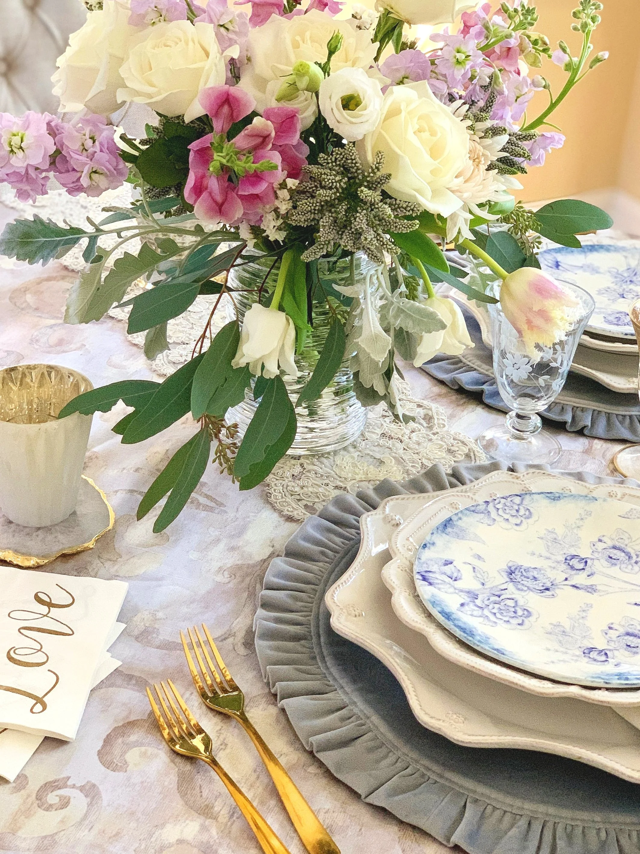 Close up of a spring Mother's Day centerpiece with pink roses parrot tulips and soft cream blooms in mixed textures in a Simon Pearce hurricane vessel
