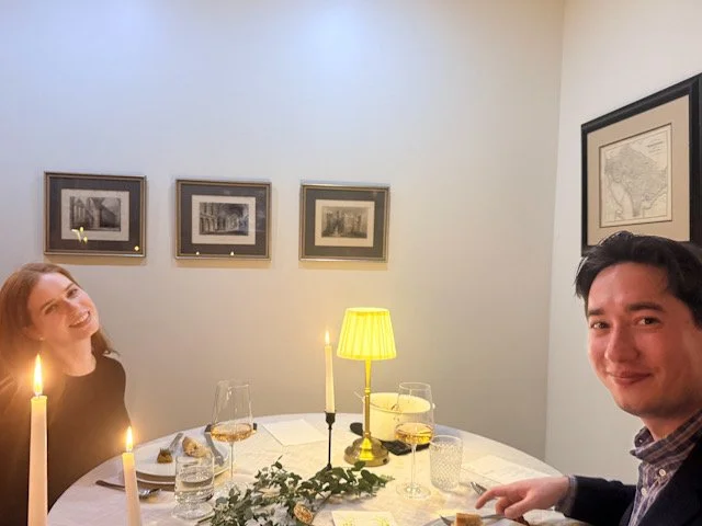 Hosts seated at the end of a long candlelit dinner table after guests have gathered.