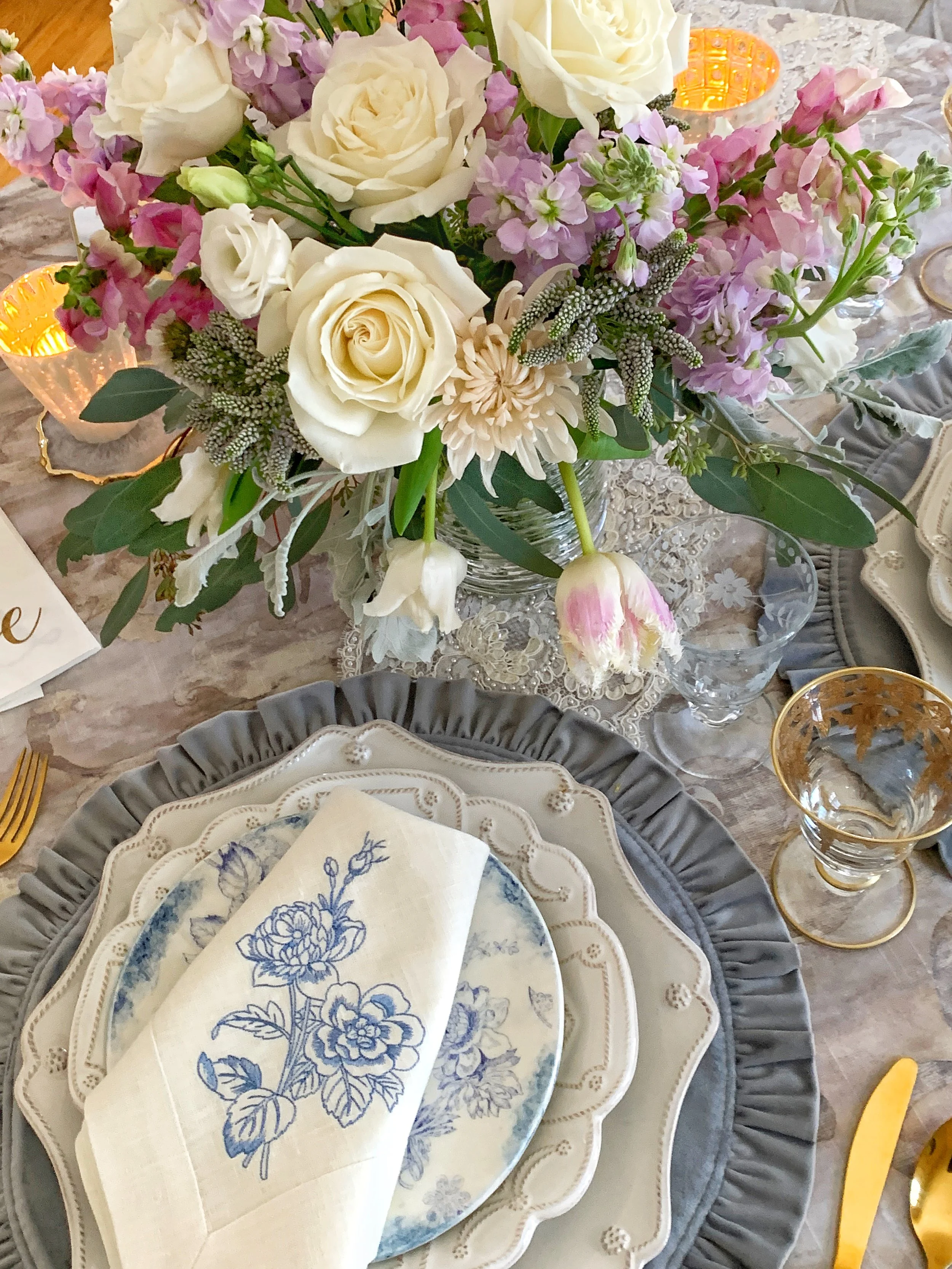 Close up of a Mother's Day place setting with Juliska Berry charger Arte Italica accent plate etched gold wine glasses gold vintage flatware and white linen napkin with French blue embroidered flower