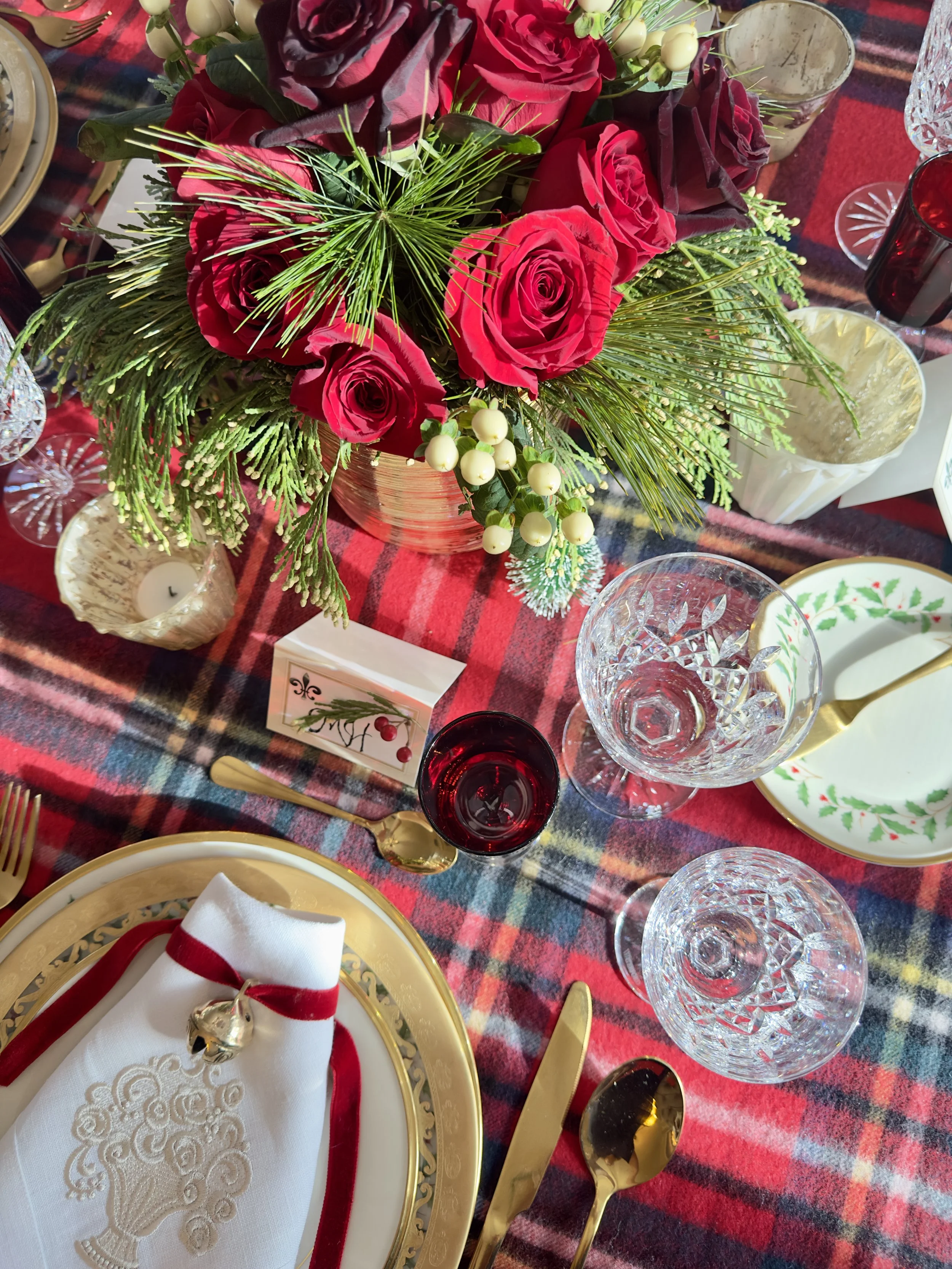 A tartan wool throw used as a tablecloth on a Christmas table with red roses, pine, and gold flatware