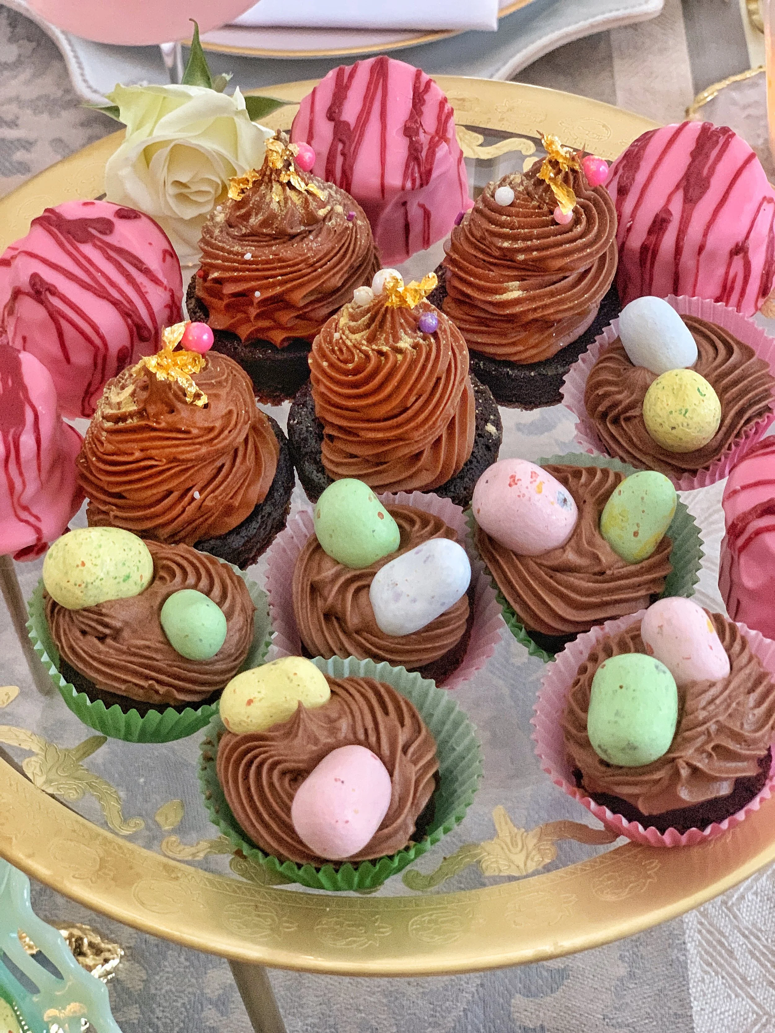 Elegant Easter dessert platter with chocolate cake, brownies, petit fours, and candy eggs styled for a spring high tea gathering.