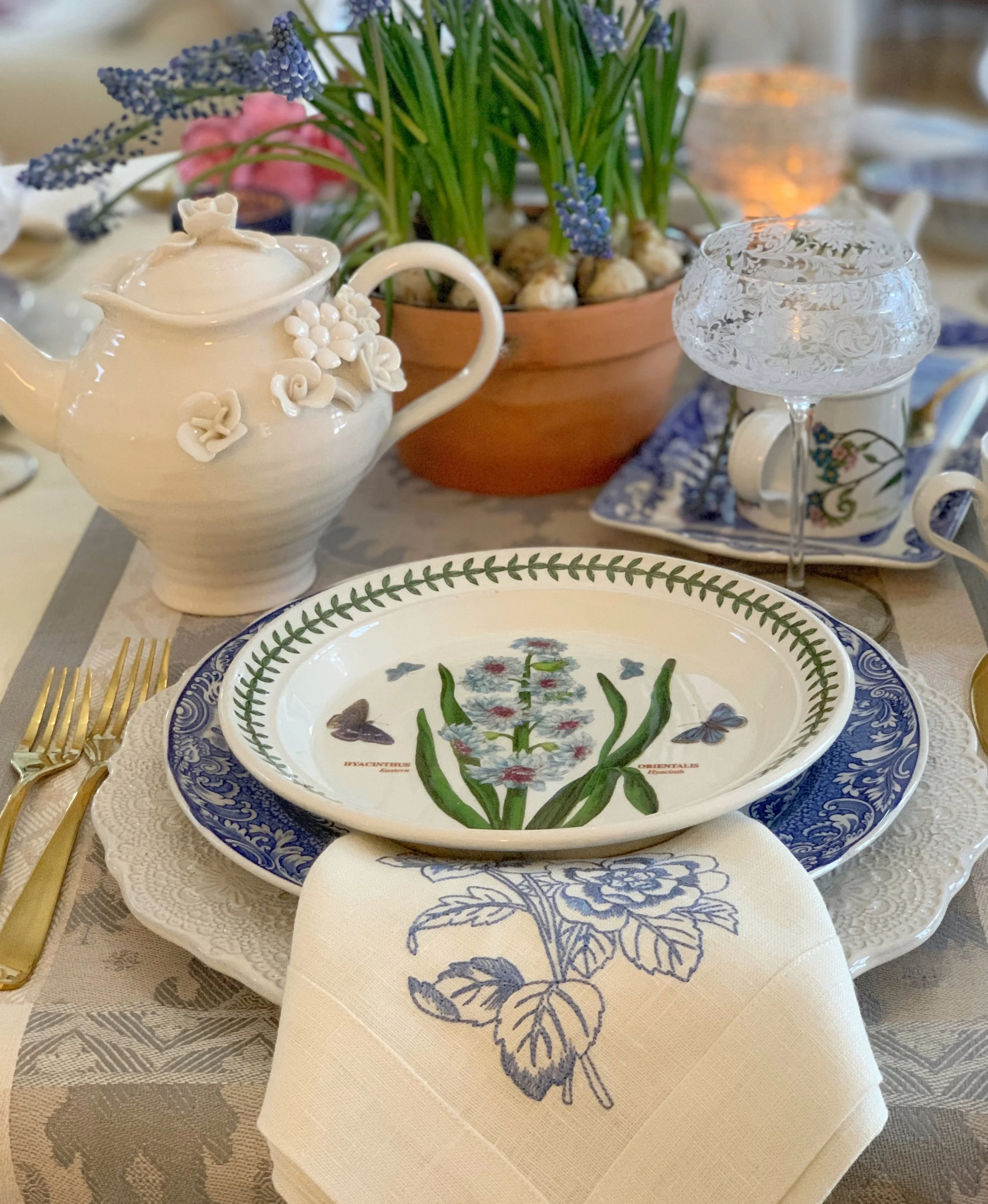 spring place setting with blue floral linen napkin cascading from layered plates with grape hyacinth centerpiece
