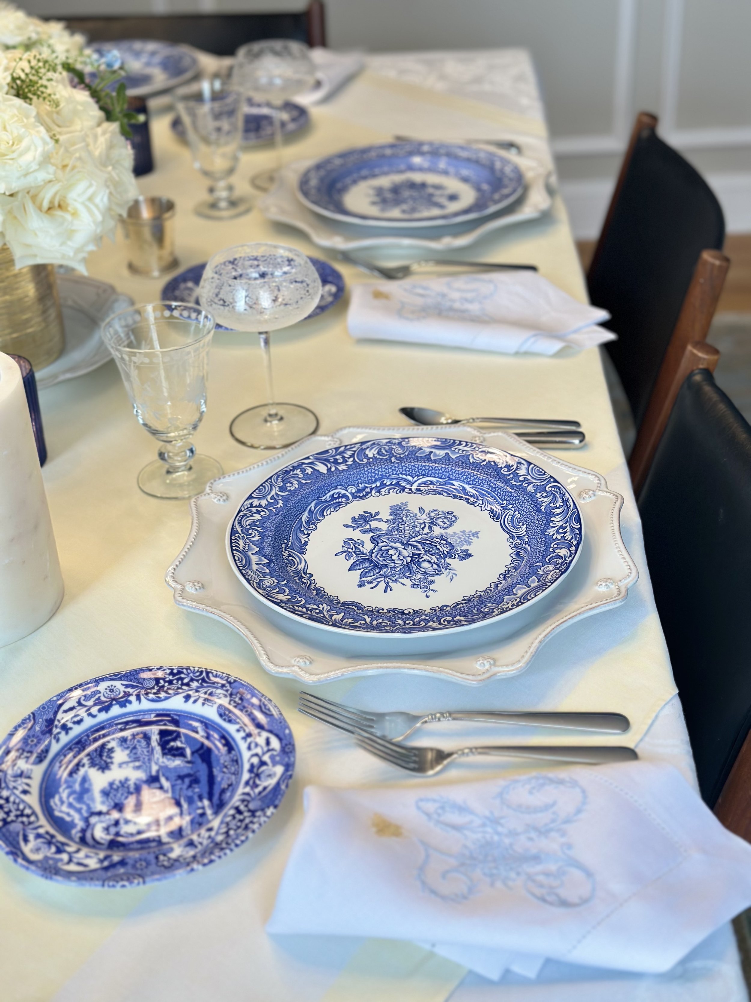 Elegant blue and white place setting with layered vintage linens, heirloom china, and soft candlelight creating a warm, welcoming table.