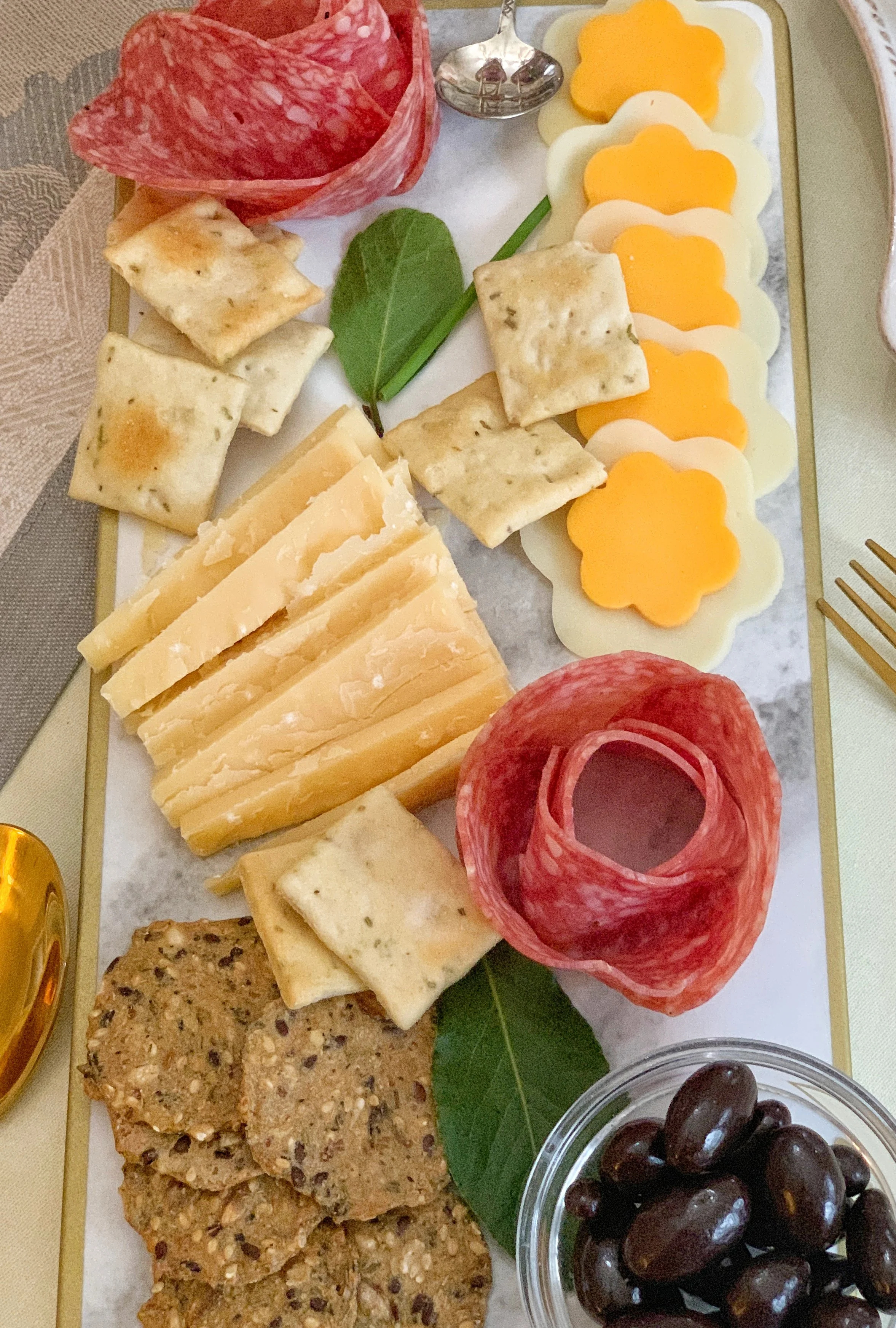 Spring Easter charcuterie board with assorted meats, cheeses, crackers, chocolate-covered almonds, and floral-shaped cheese details styled for a high tea gathering.