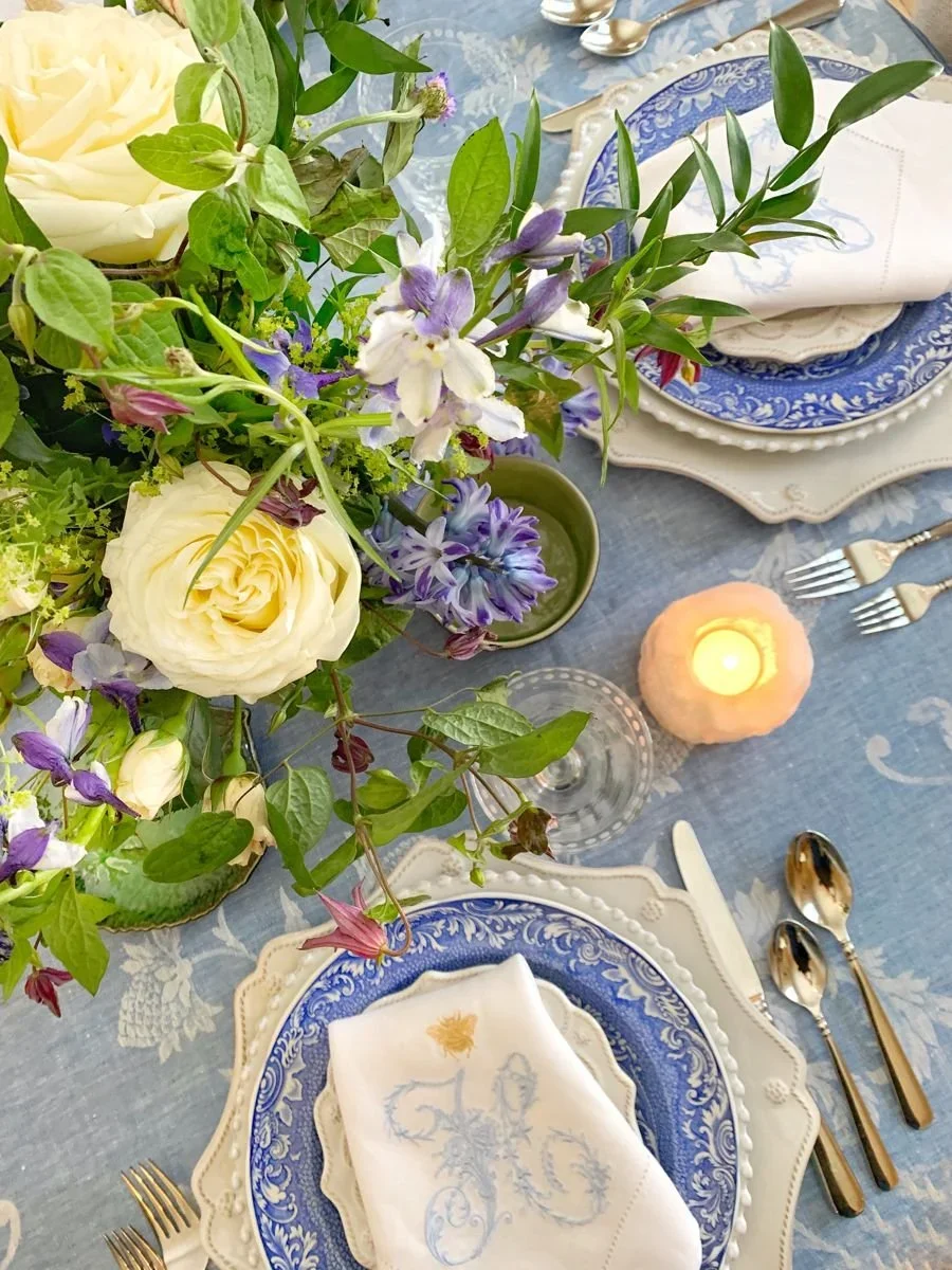 French coastal table setting with blue and white plates, a monogrammed linen napkin, and candlelight