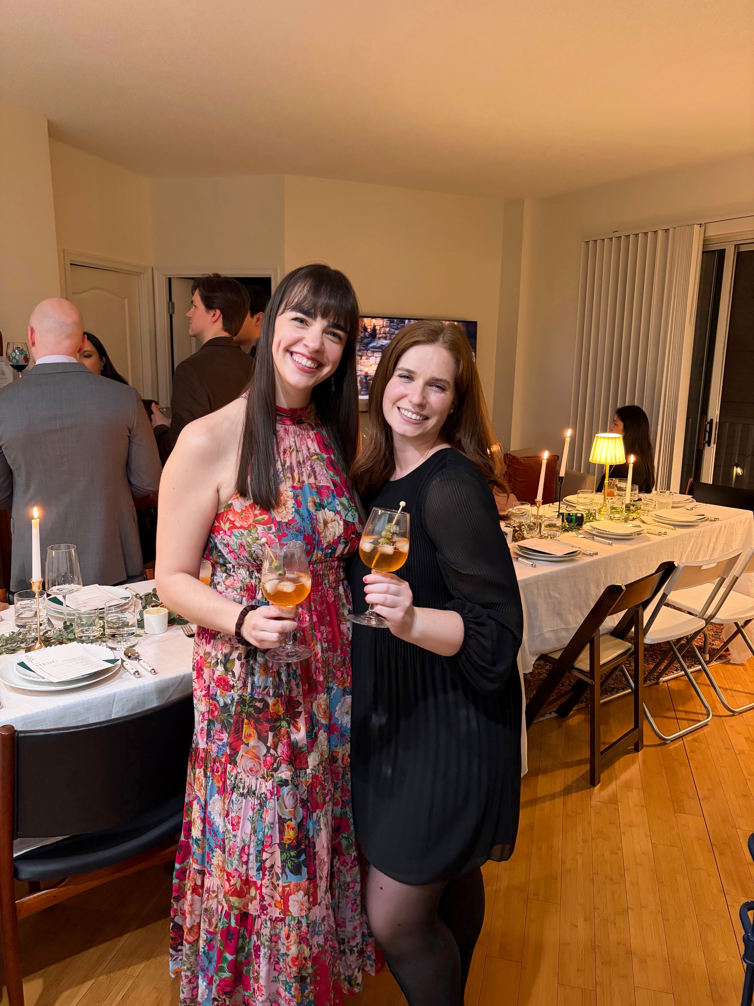 Two women standing beside a fully set candlelit dining table before hosting fifteen guests in a Washington condominium.