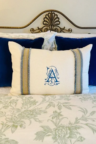 Layered bedding with a toile duvet, a monogrammed pillow, a chinoiserie pillow, and deep blue velvet pillows.