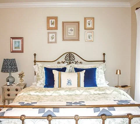 A gallery wall of framed pressed flowers gathered from a home garden, arranged above a vintage iron bed.