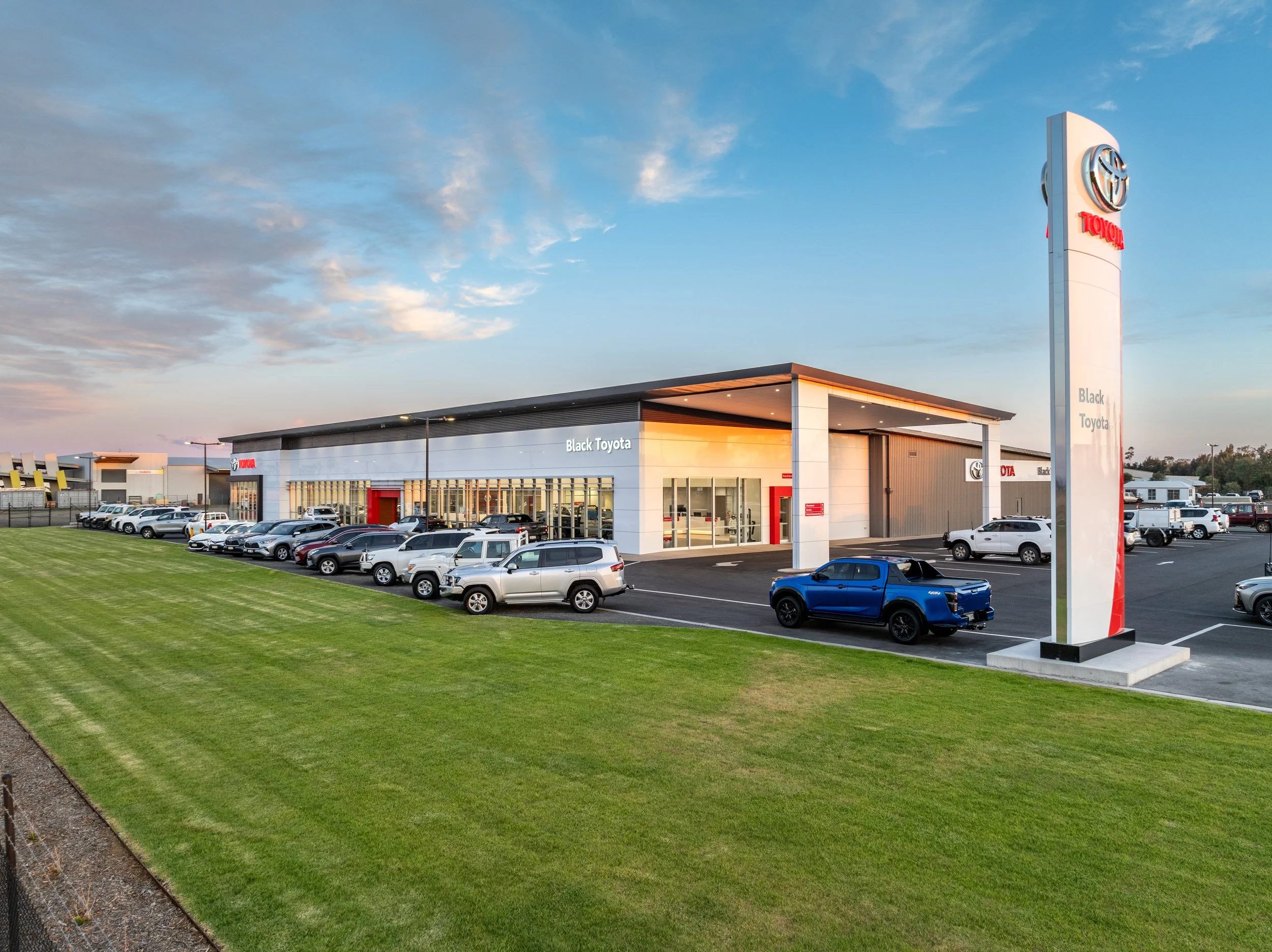 Exterior view of Black Toyota car dealership with numerous parked vehicles on a clear day with blue sky and a few clouds.