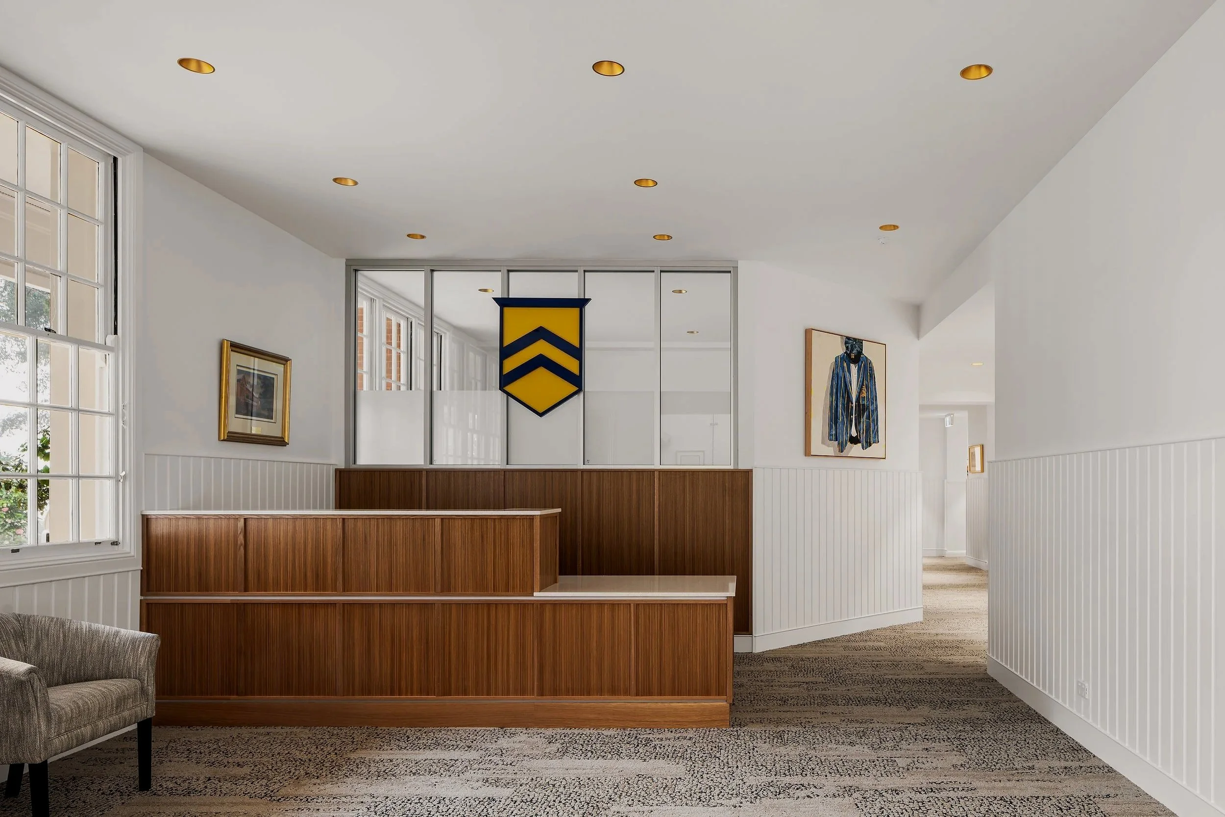 A modern interior with white walls and wood paneling, featuring paintings, windows, a beige armchair, and a decorative banner with yellow and blue chevrons.