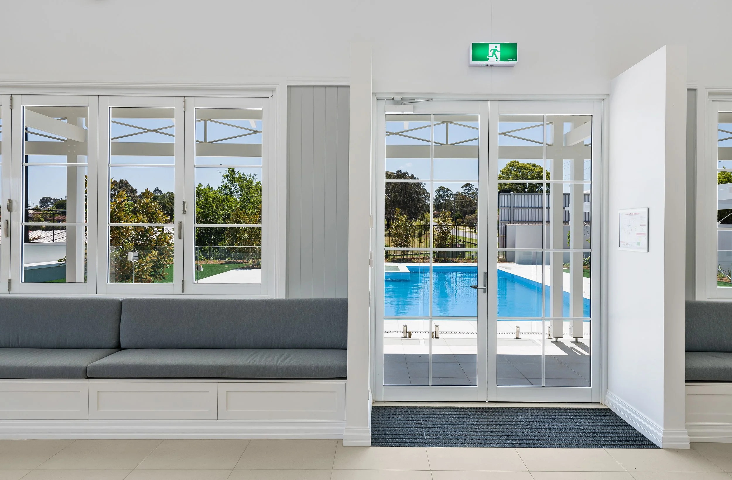 Indoor waiting area with gray bench seating, large windows, and a view of a swimming pool outside.