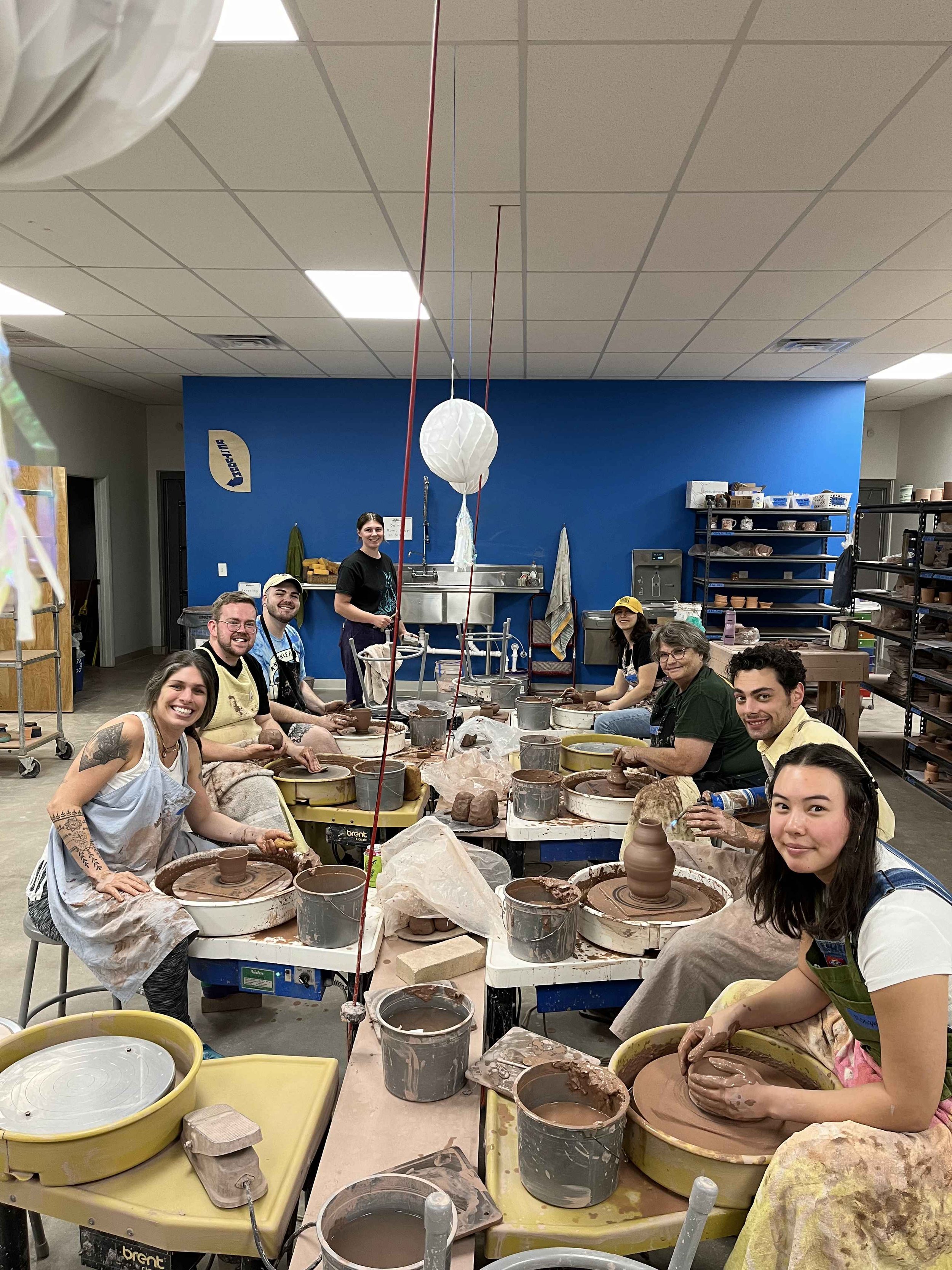 Eight people, three men and five women smiling at the camera while working on the wheel