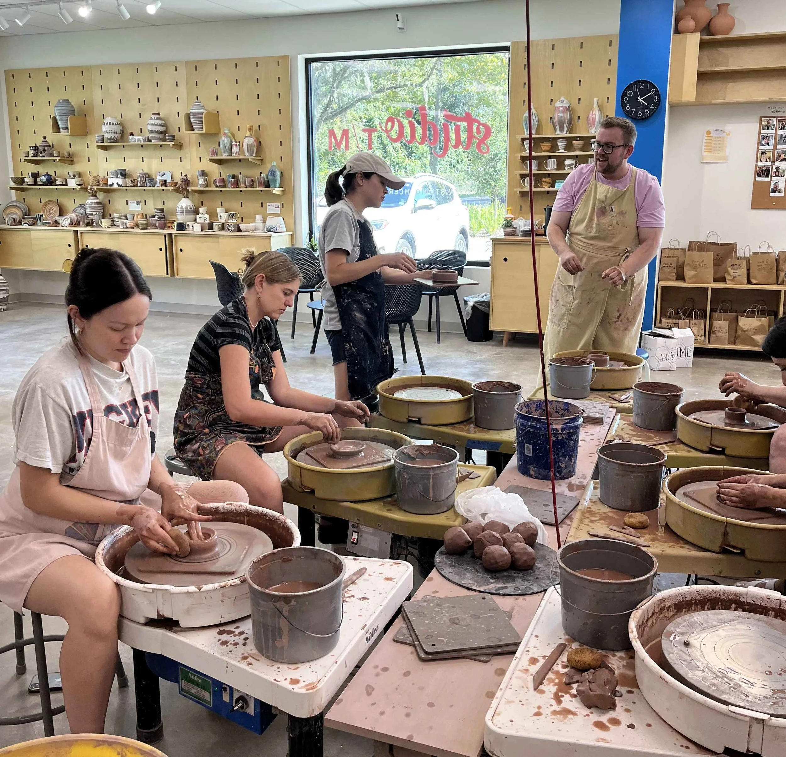 A man, three women, and two sets of hands throwing on the pottery wheel