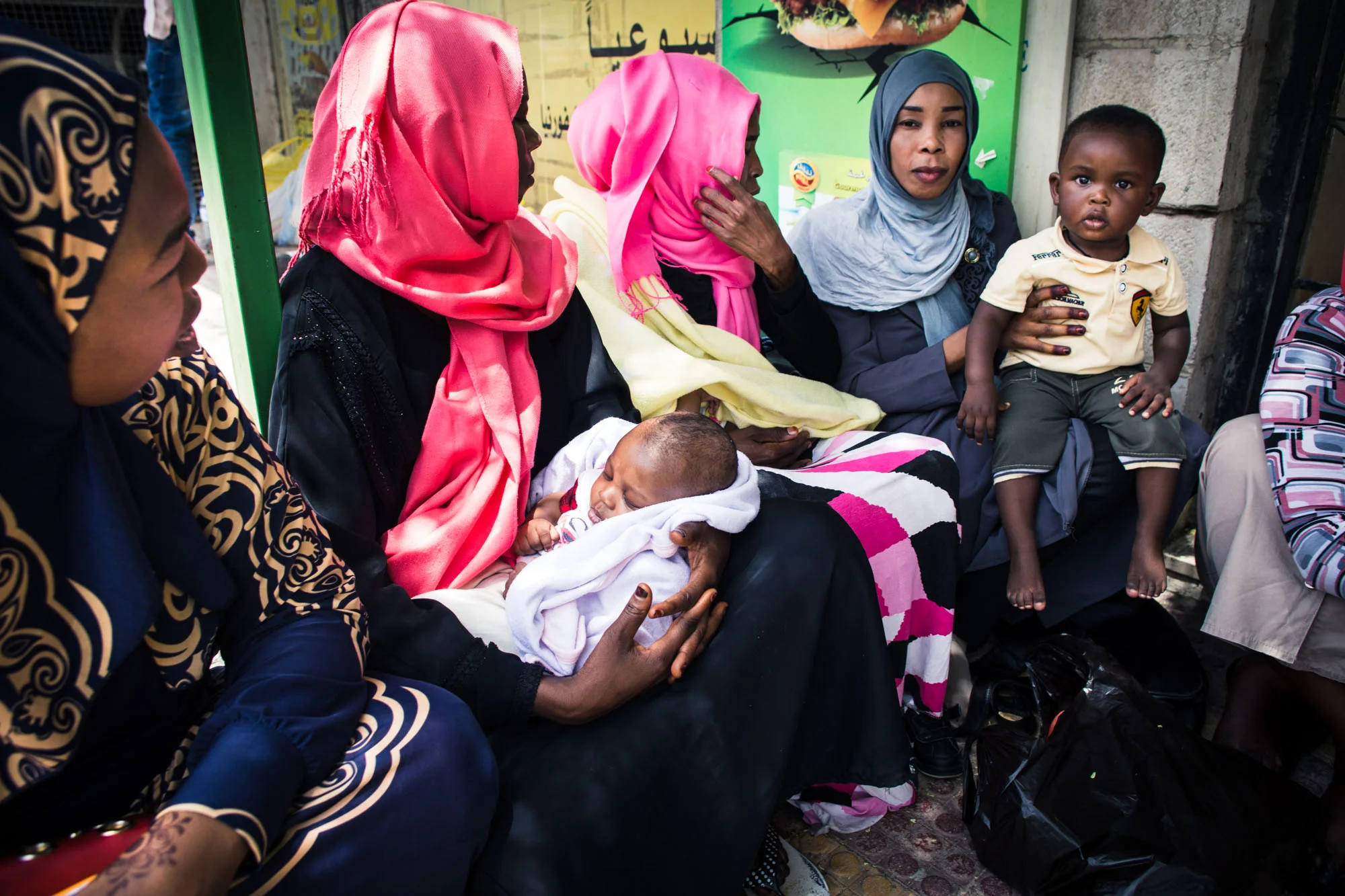 Sudanese women wait with their children outside a supermarket for their turn to purchase groceries through Collateral Repair Project's food voucher program for refugees in Amman.