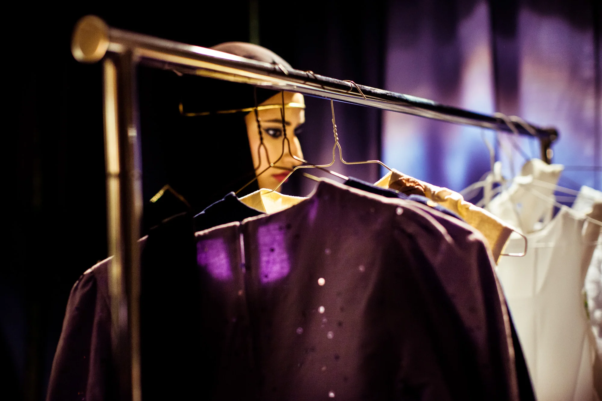 Backstage, a model browses through a clothing rack, looking for accessories.