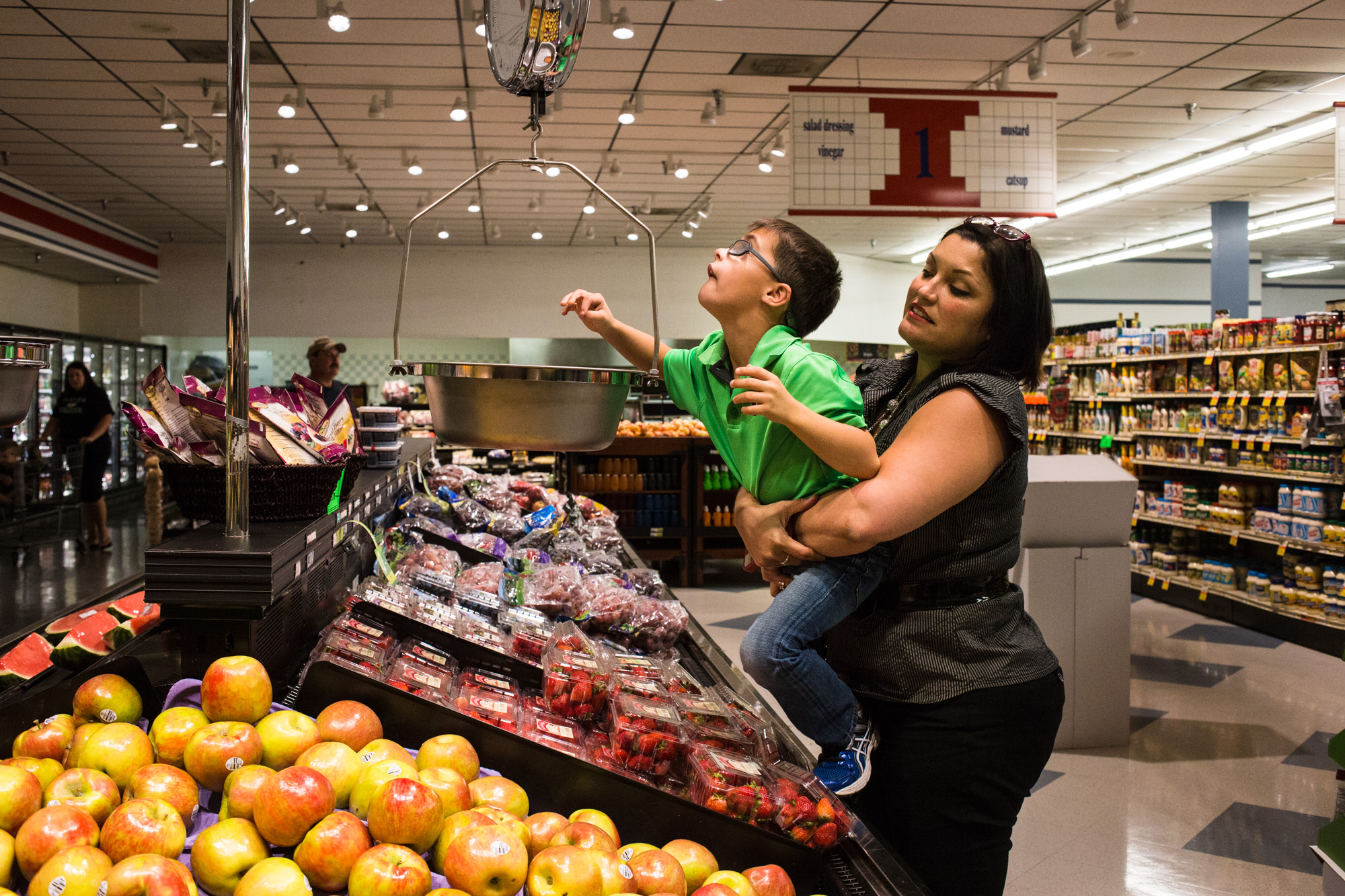 Bettina holds Treven up in the grocery store so he can weigh an apple.