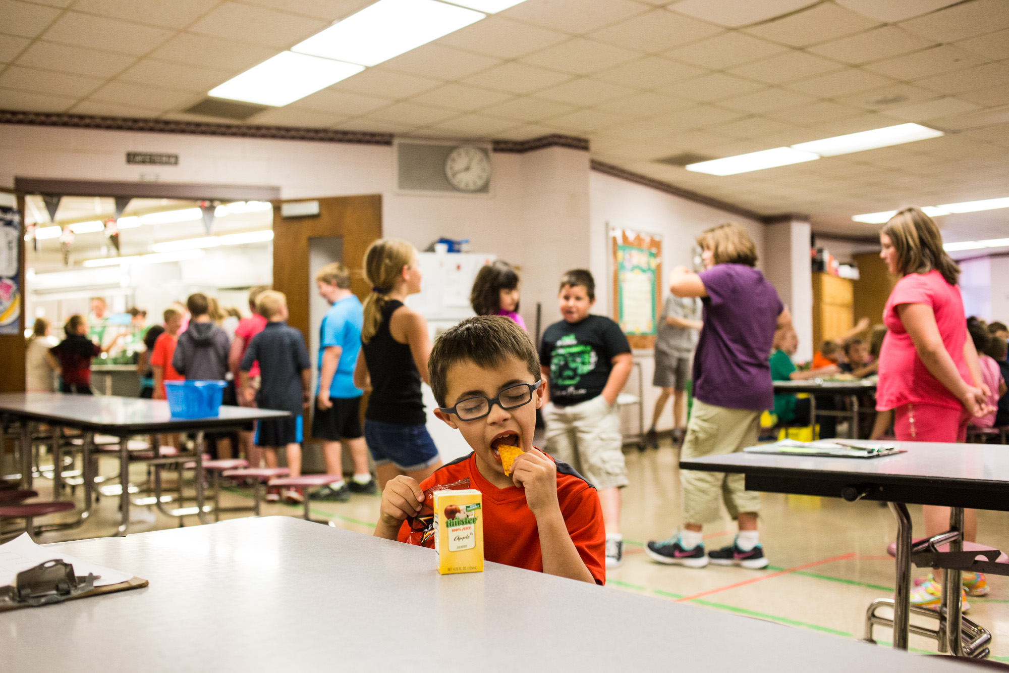 Treven starts eating his lunch he brought from home while his classmates stand in line at the cafeteria.