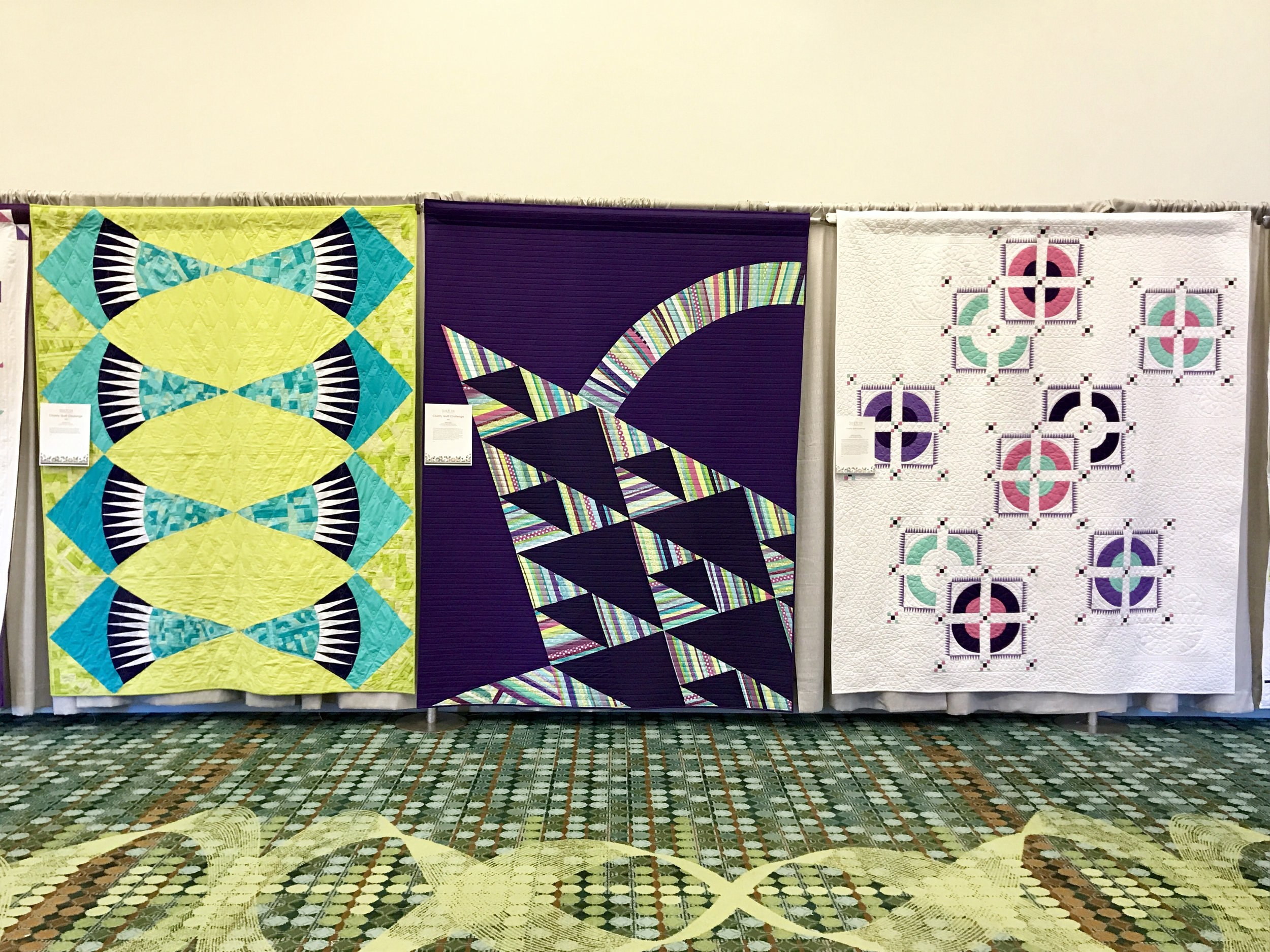 Our modern basket quilt (center) hangs at QuiltCon between quilts made by Knoxville MQG (left) and Music City MQG (right).