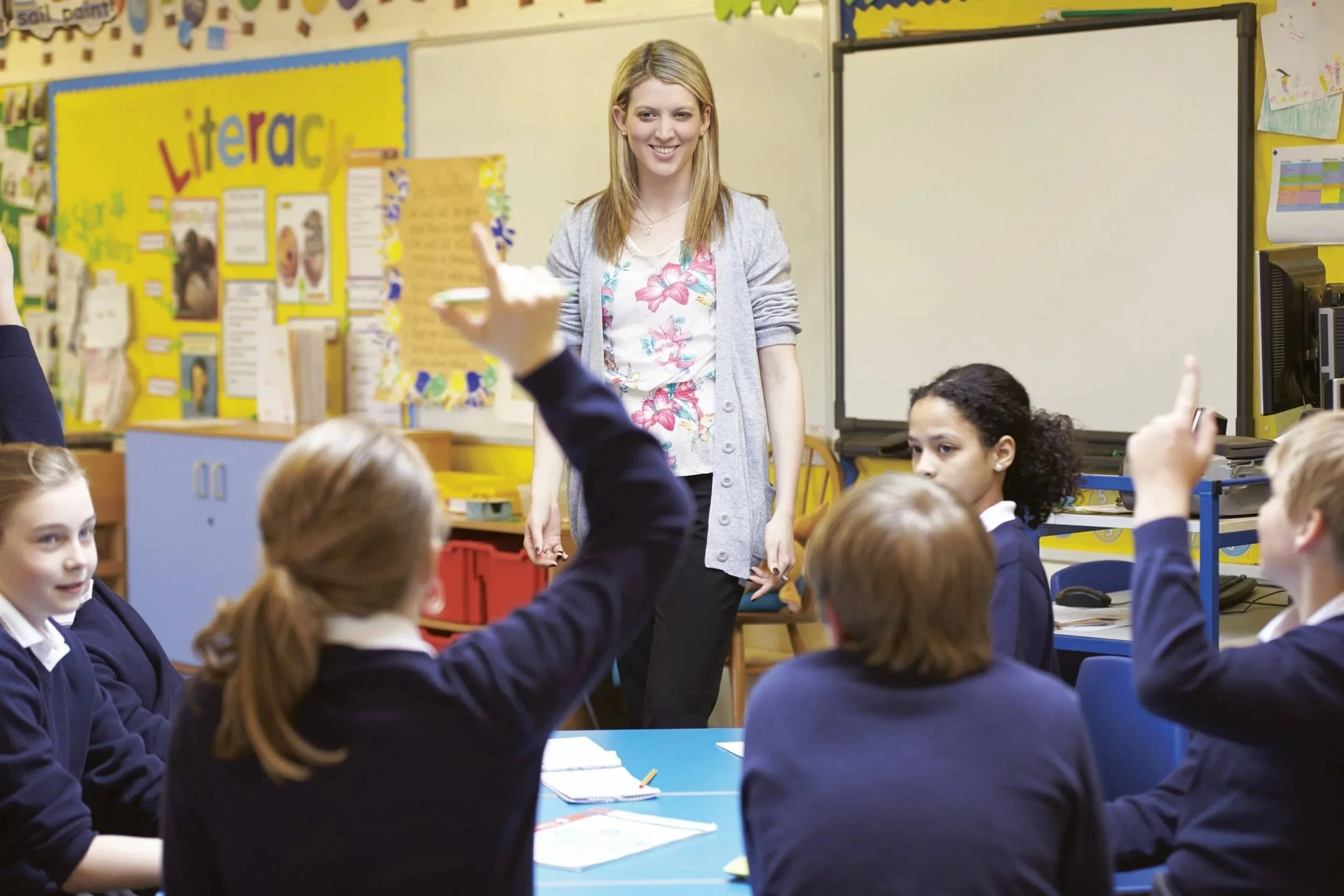 KS2 children in a kindness assembly with hands raised, teacher at the front